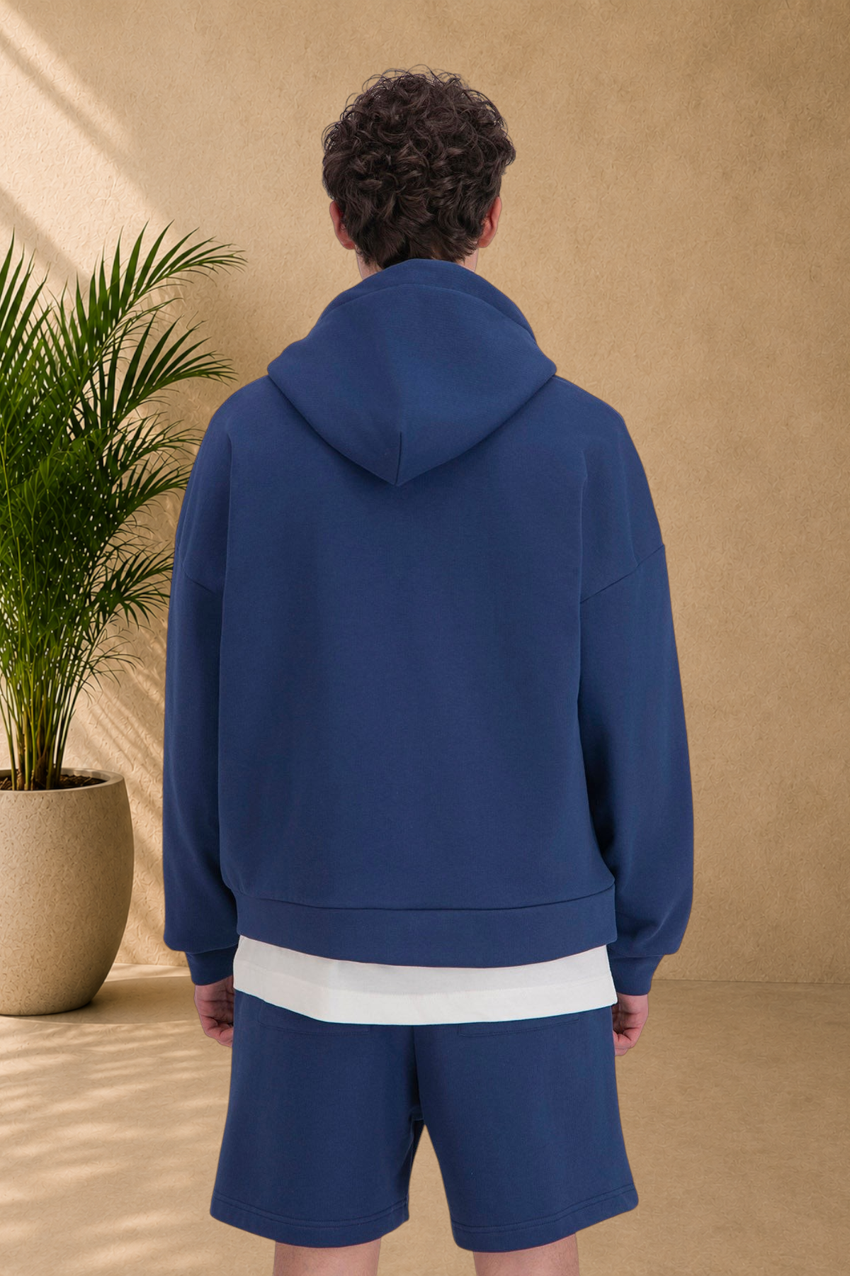 Back view of a model wearing a Stayin blue quilted zip-up hoodie with a white shirt underneath