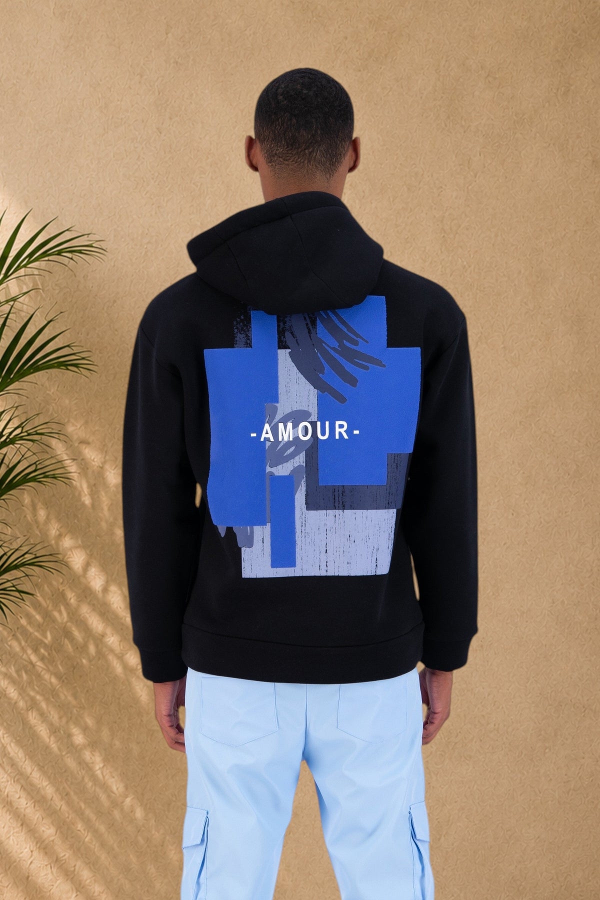 Stayin black hooded sweatshirt with blue graphic Amour print on the back, worn by a model in light blue cargo pants