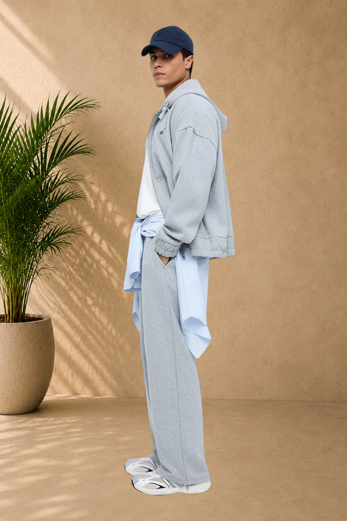 Stayin grey Oxford jacket worn by a model with matching sweatpants, a cap, and a light blue shirt tied at the waist.