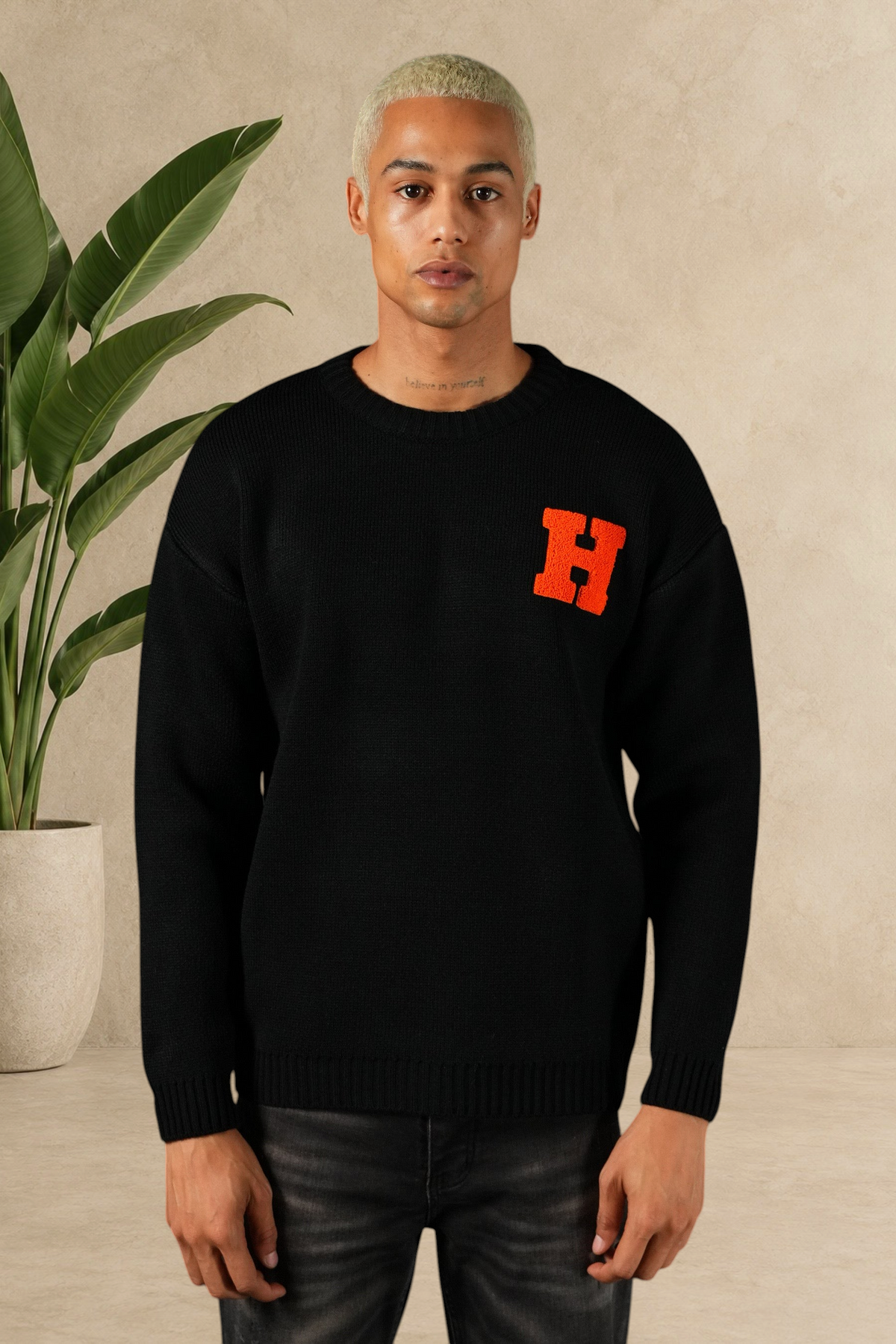 Mannequin portant un pull Stayin noir en maille épaisse avec un logo H orange sur la poitrine