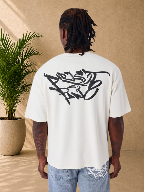 Stayin beige oversized cotton t-shirt with large black graffiti graphic print on the back, worn by a man.