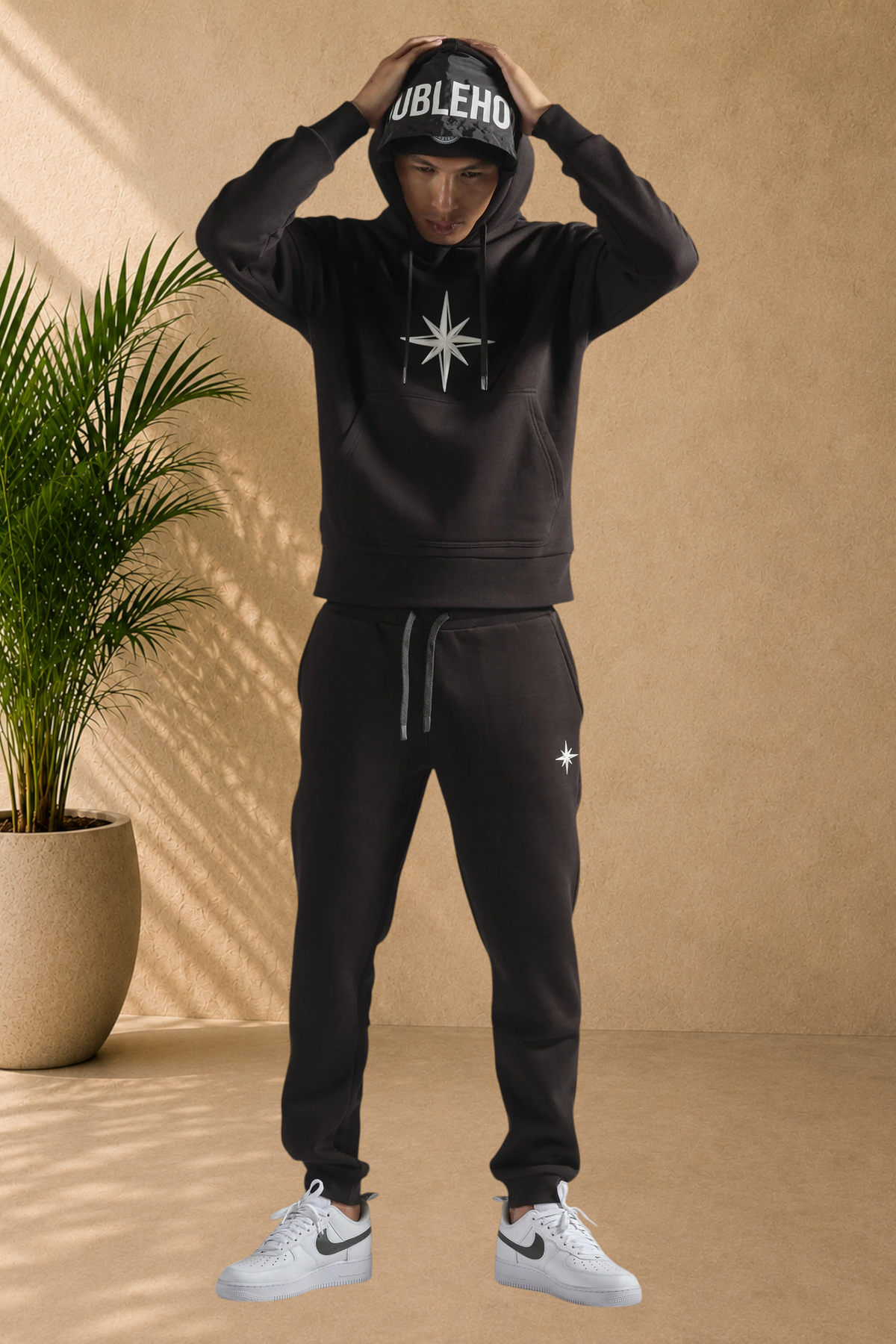 Stayin black doublehood sweatshirt with star graphic and matching joggers worn by a model in a studio setting