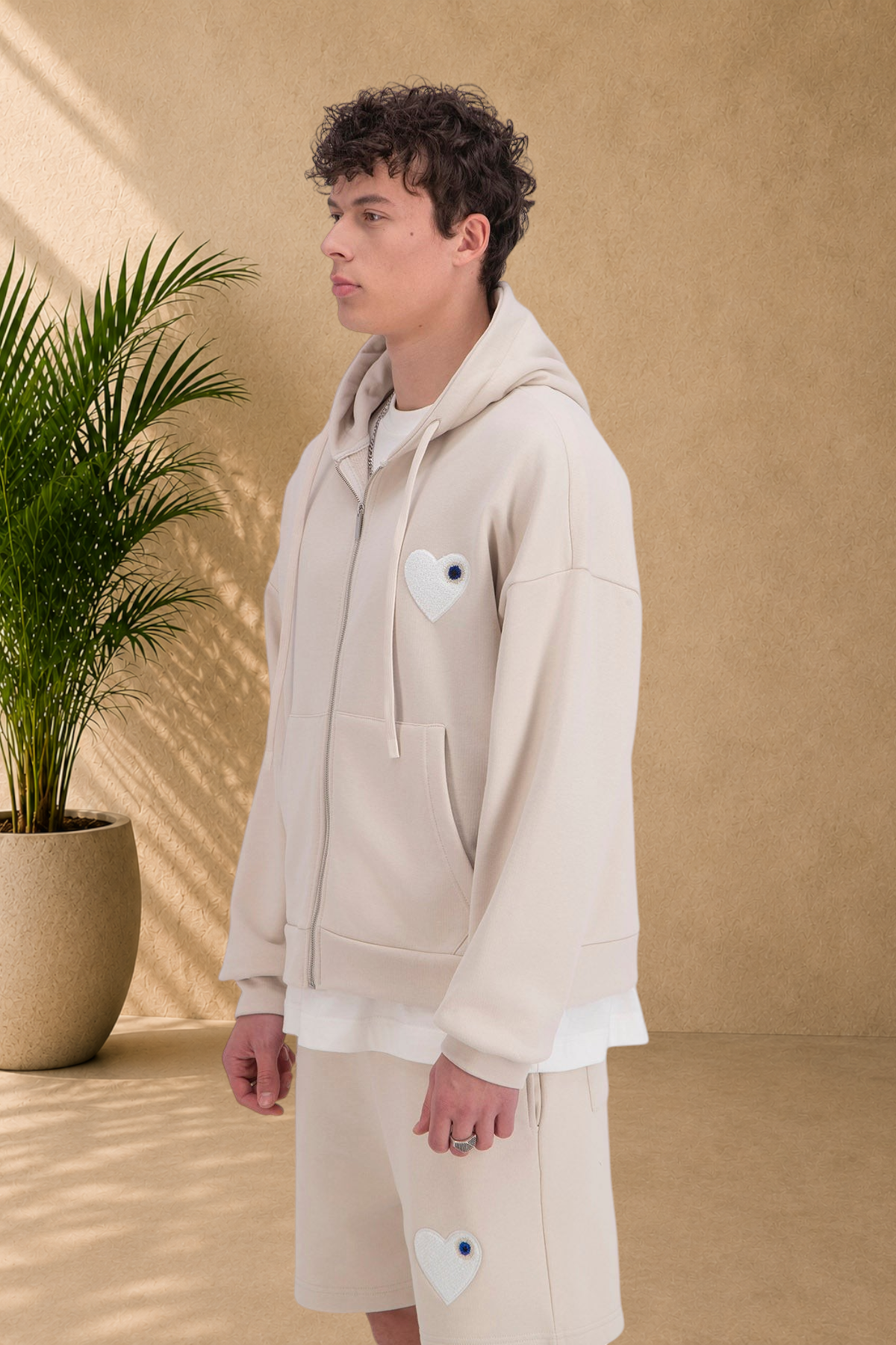 Stayin beige quilted zip-up hoodie with white heart patch worn by a male model in profile view