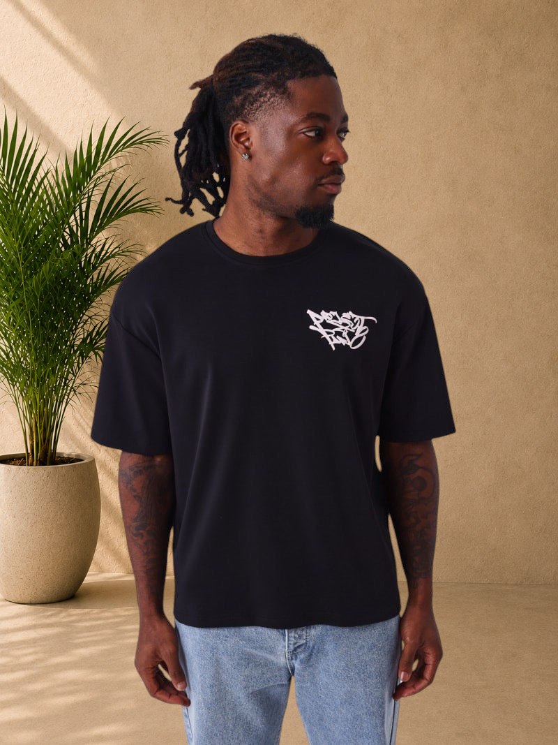 Stayin PXP black oversized cotton t-shirt with white graffiti logo on chest worn by a man