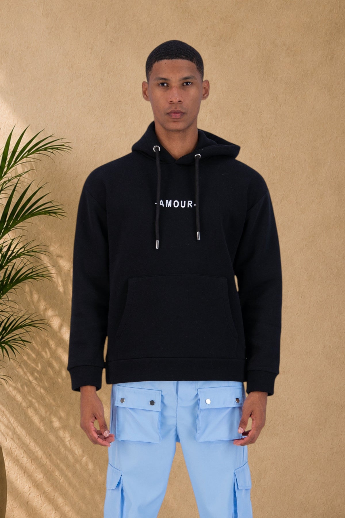 Stayin black quilted hoodie with Amour text on chest worn by a male model with light blue cargo pants