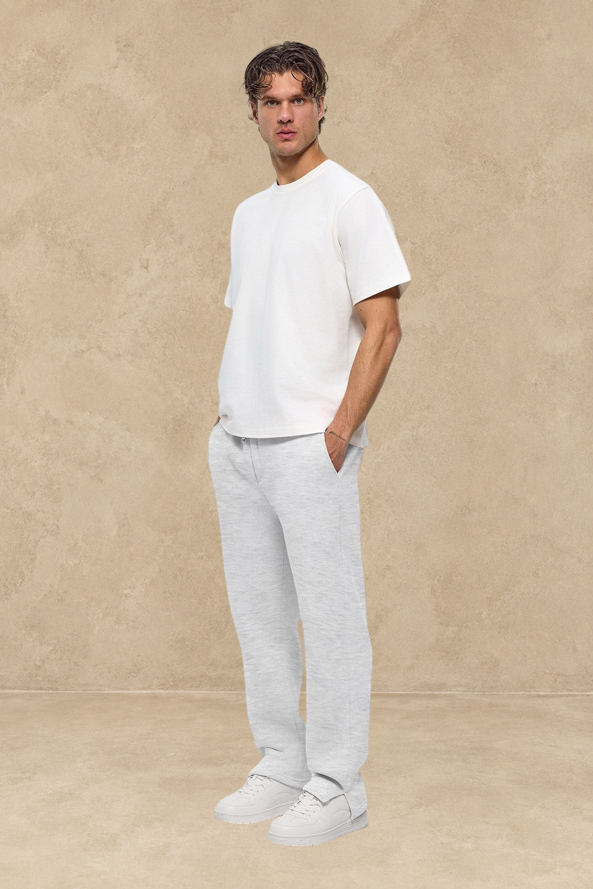 Homme portant un pantalon jogg gris Stayin avec fente à la cheville et t-shirt blanc sur fond blanc