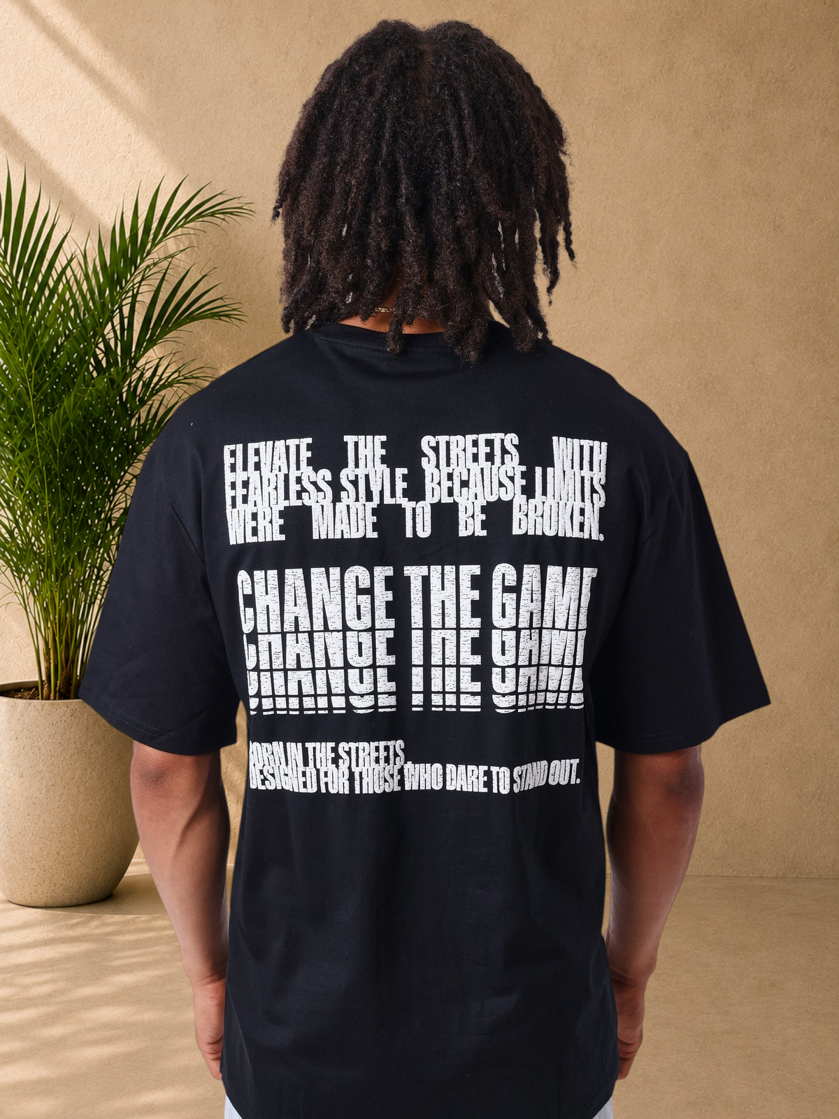 Stayin PXP black cotton t-shirt with white distressed typographic print on the back worn by a man with dreadlocks