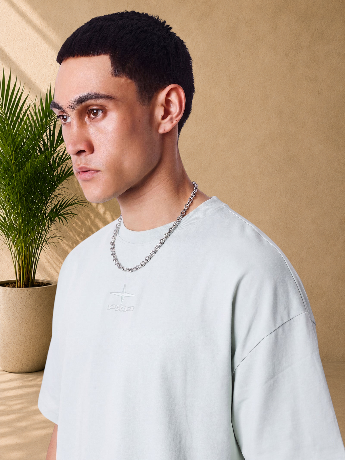 Stayin PXP mint green boxy cotton t-shirt with tonal embossed logo on chest, worn by a model with a silver chain.