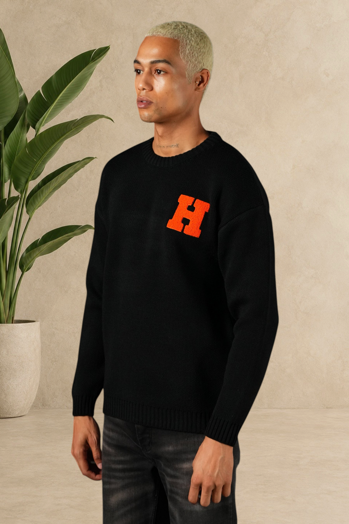 Mannequin portant un pull Stayin noir en maille épaisse avec un grand H orange brodé sur la poitrine
