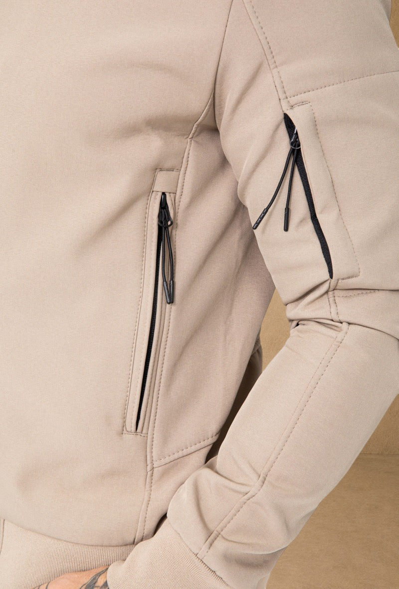 Stayin beige hooded windbreaker jacket with black zippered sleeve and side pockets, close-up view