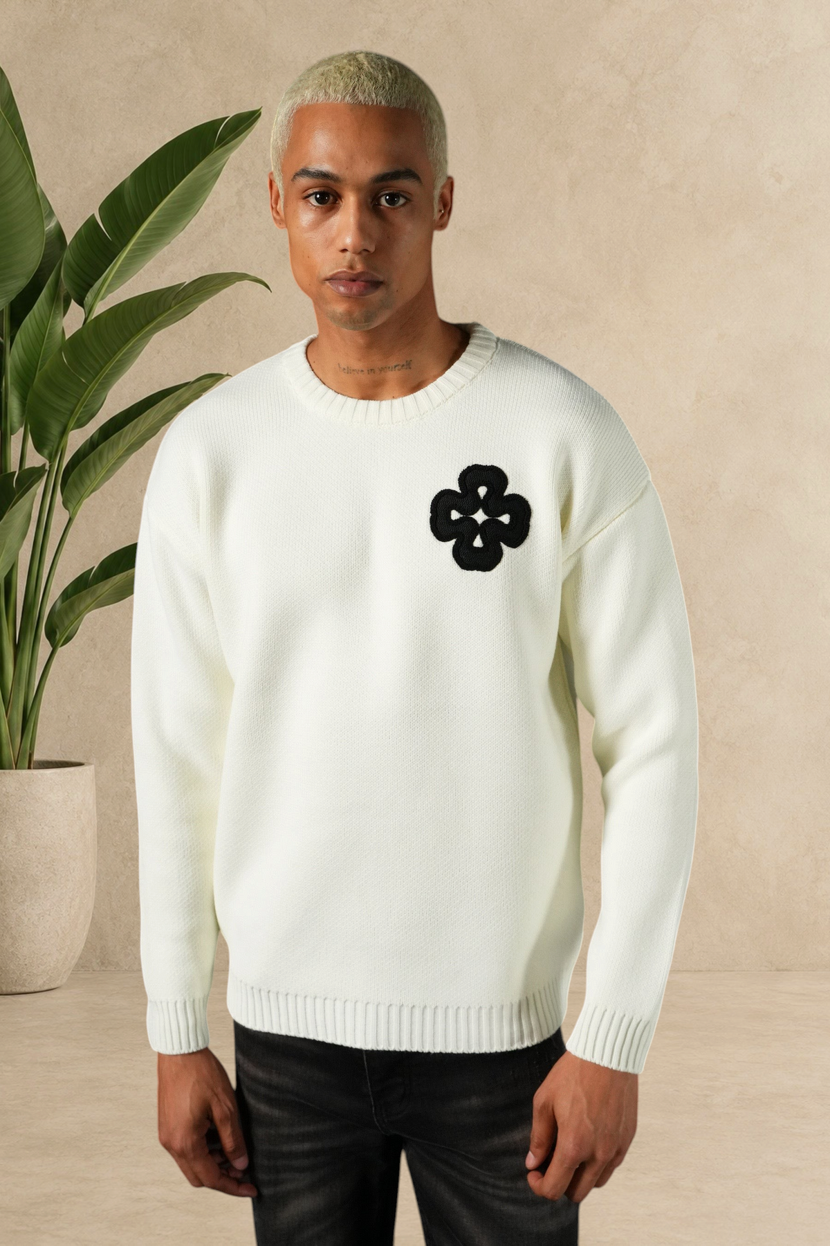 Mannequin portant un pull Stayin blanc en maille épaisse avec un motif trèfle noir sur la poitrine