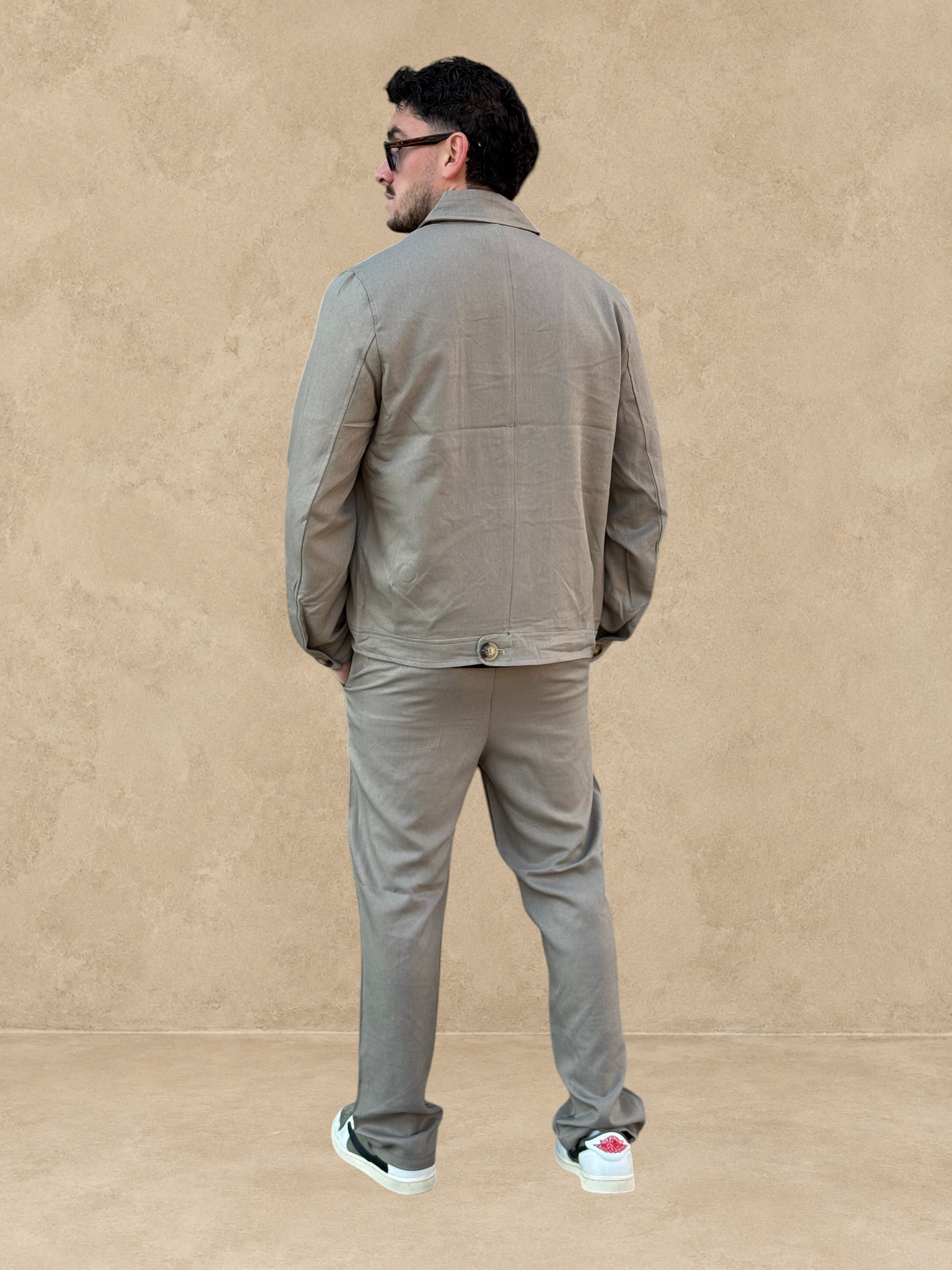 Homme portant un ensemble Stayin beige foncé avec veste zippée décontractée et pantalon droit, vue de dos