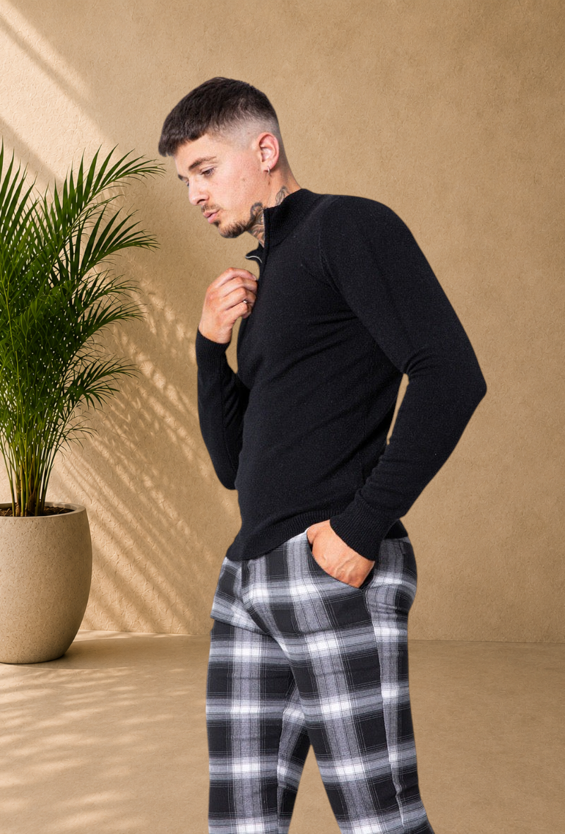 Stayin black zip-up mock neck sweater worn by a man with plaid trousers in a bright studio setting