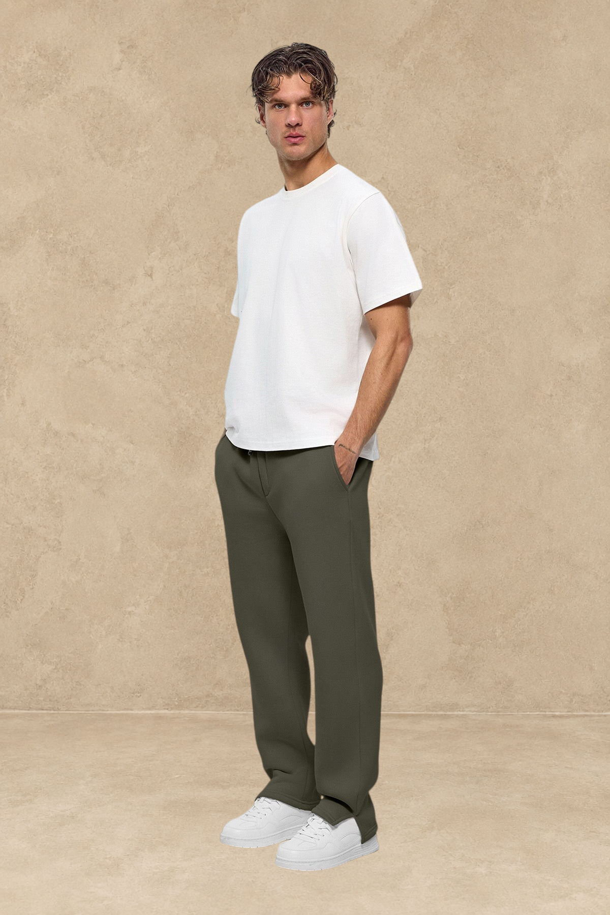 Homme portant un pantalon jogg kaki Stayin avec fente à la cheville et t-shirt blanc sur fond neutre