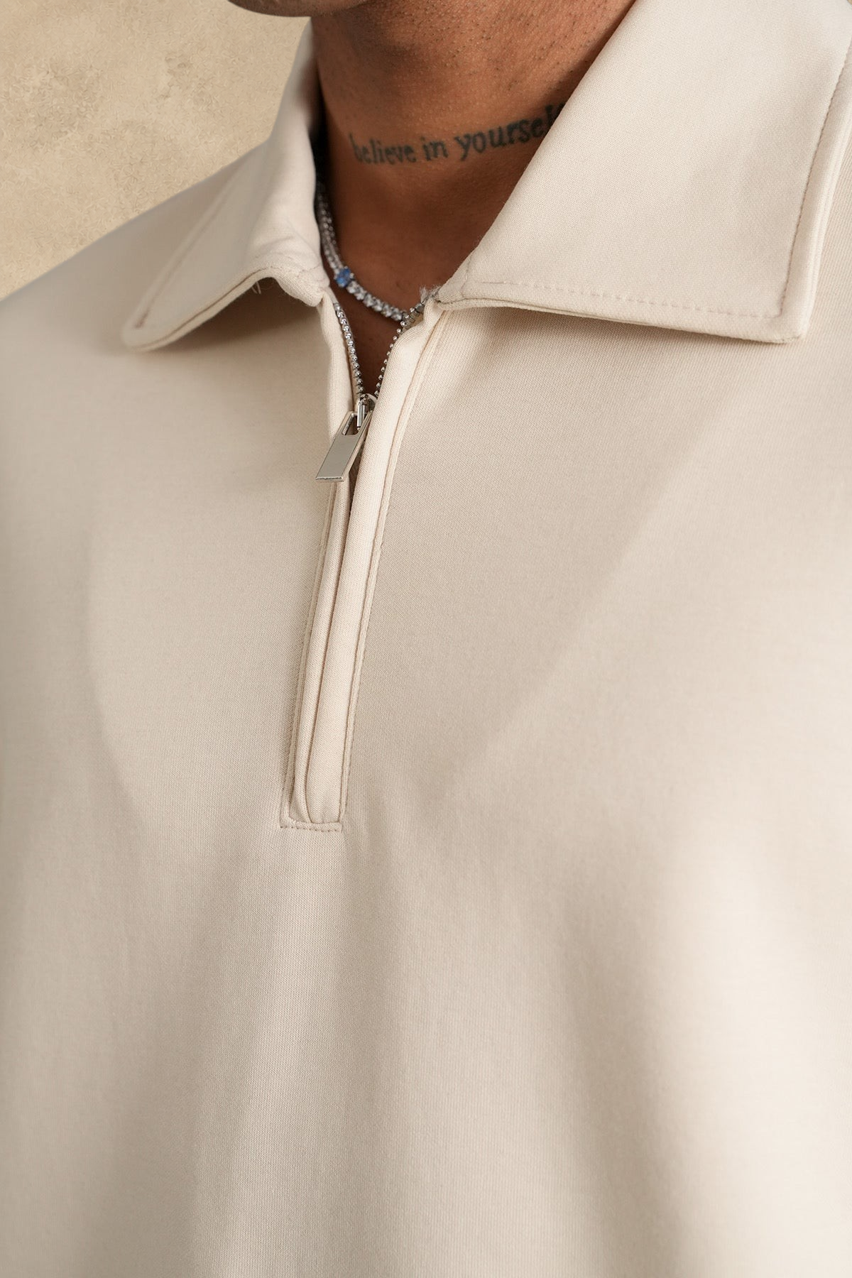 Gros plan sur un polo beige Stayin à col zippé en polyester, porté par un mannequin.