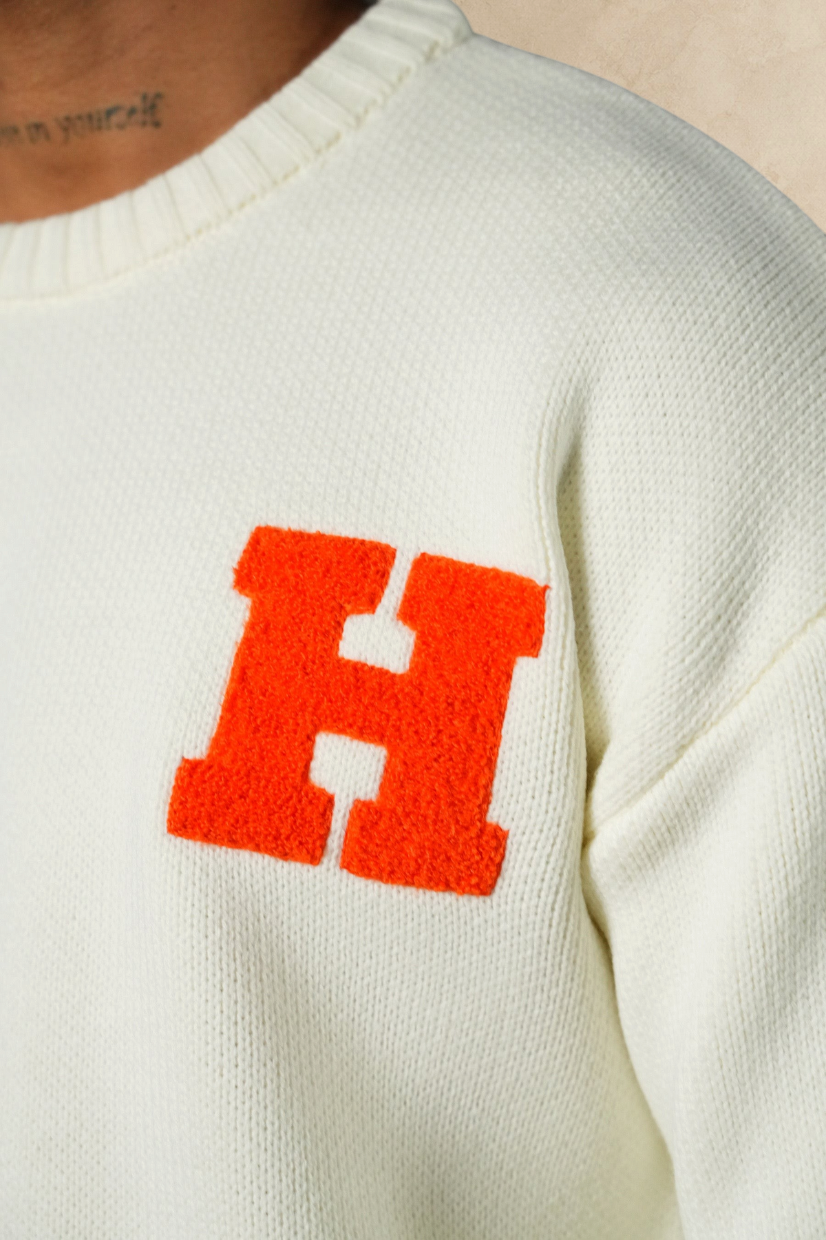 Pull Stayin blanc en maille épaisse avec une lettre H orange brodée sur la poitrine, col rond et coupe droite.