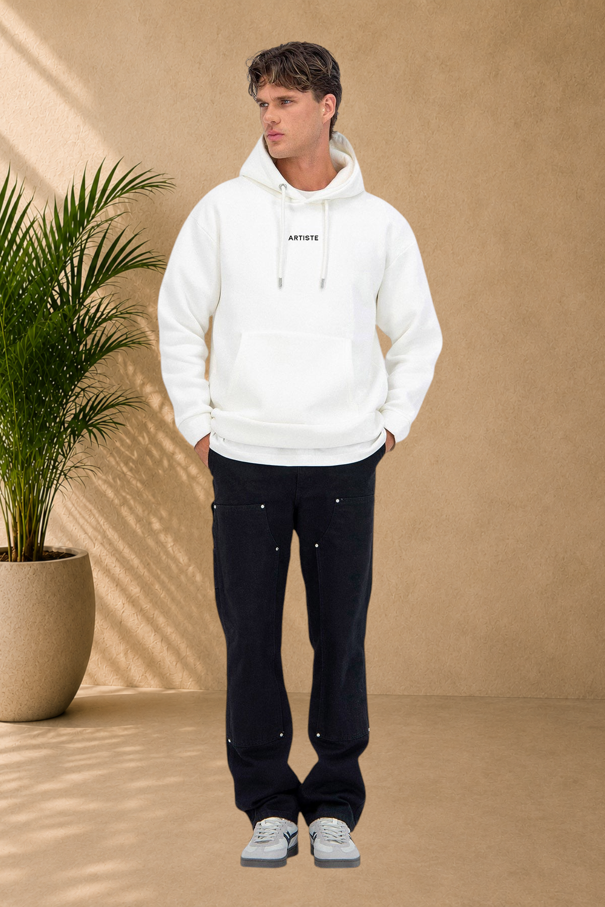 Stayin white quilted hoodie with ARTISTE print worn by a male model against a beige wall with a potted plant