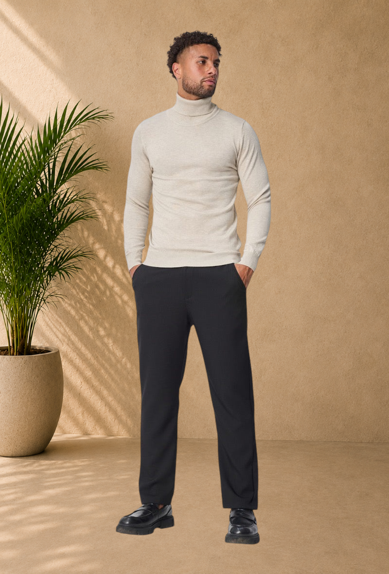 Stayin model wearing a beige slim-fit turtleneck sweater with black trousers and loafers in a studio setting.