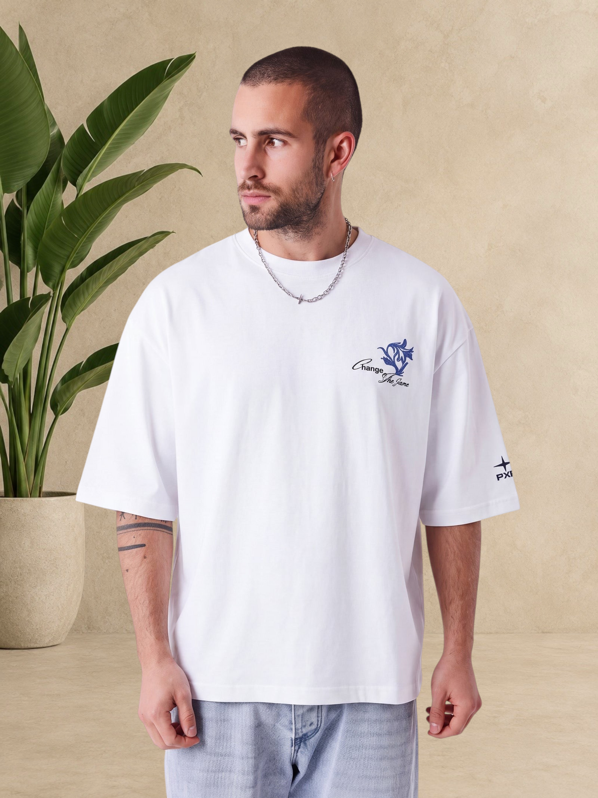 Homme portant un t-shirt blanc Stayin coupe boxy en coton avec imprimé floral bleu sur la poitrine et logo manche