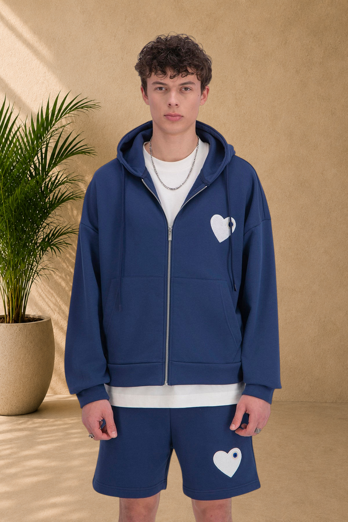Stayin blue zip-up hoodie with a white heart logo worn by a male model in a studio setting