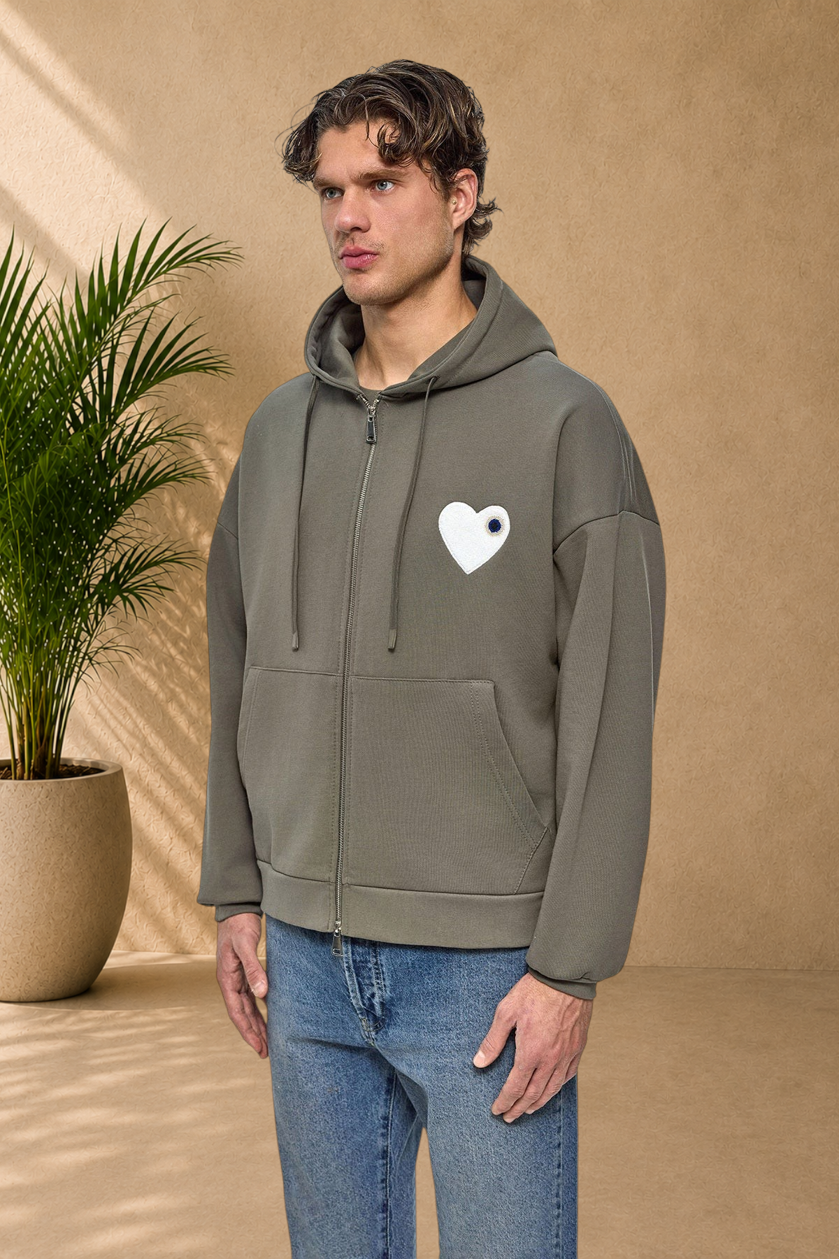 Stayin khaki zip-up hoodie featuring a white heart patch on the chest, worn by a male model on a white background.