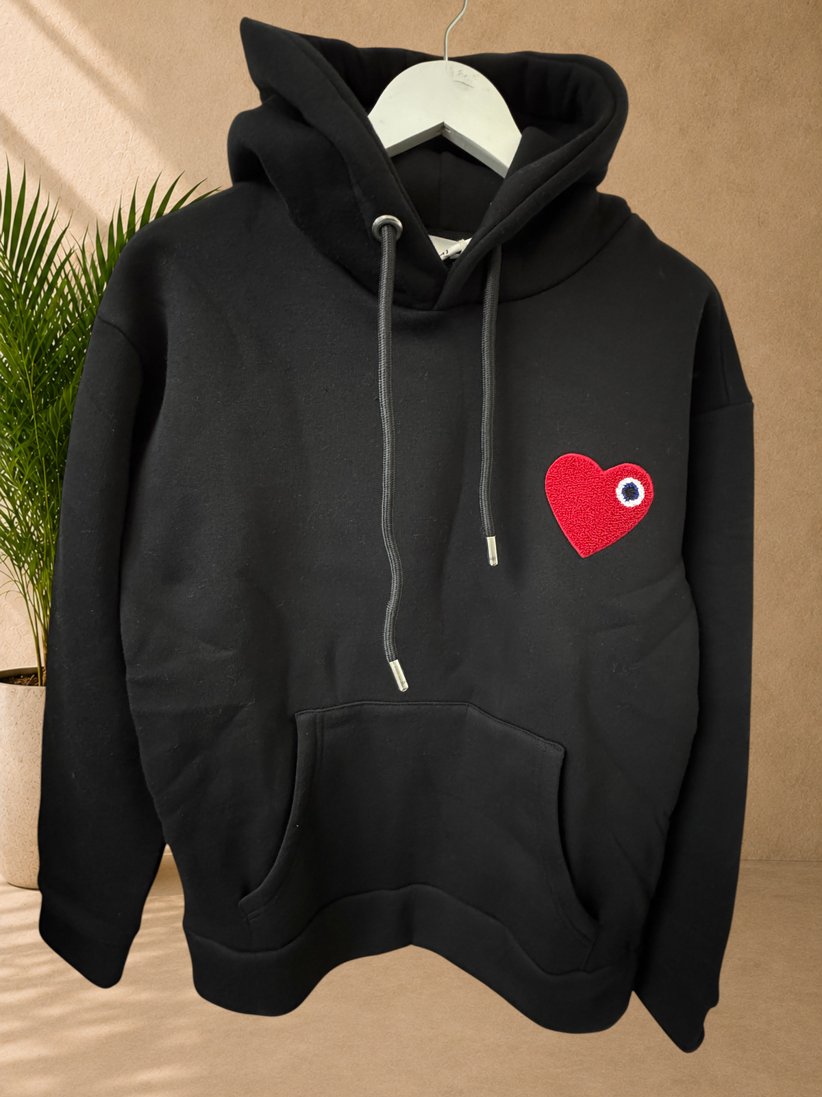 Stayin black hooded sweatshirt with a textured red heart patch featuring a blue and white eye detail on the chest