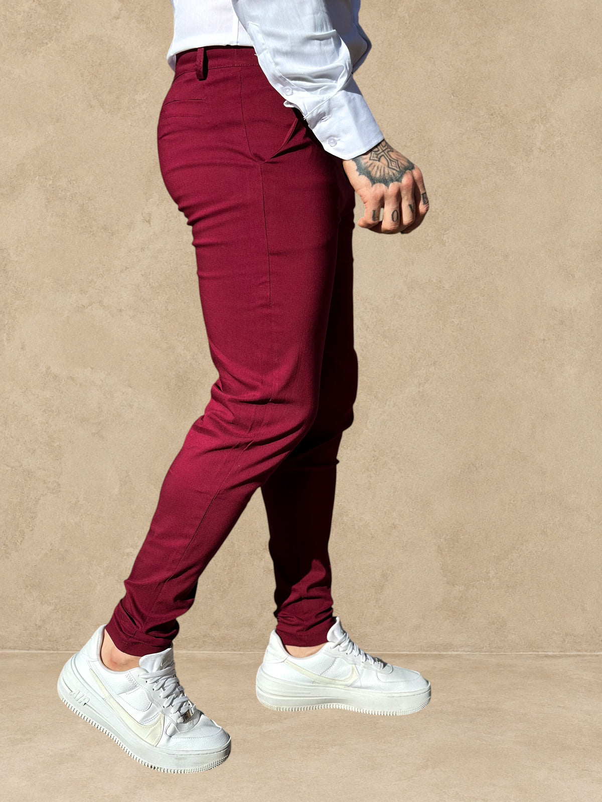 Pantalon Stayin bordeaux à coupe cintrée et style pince porté par un homme avec des baskets blanches en extérieur