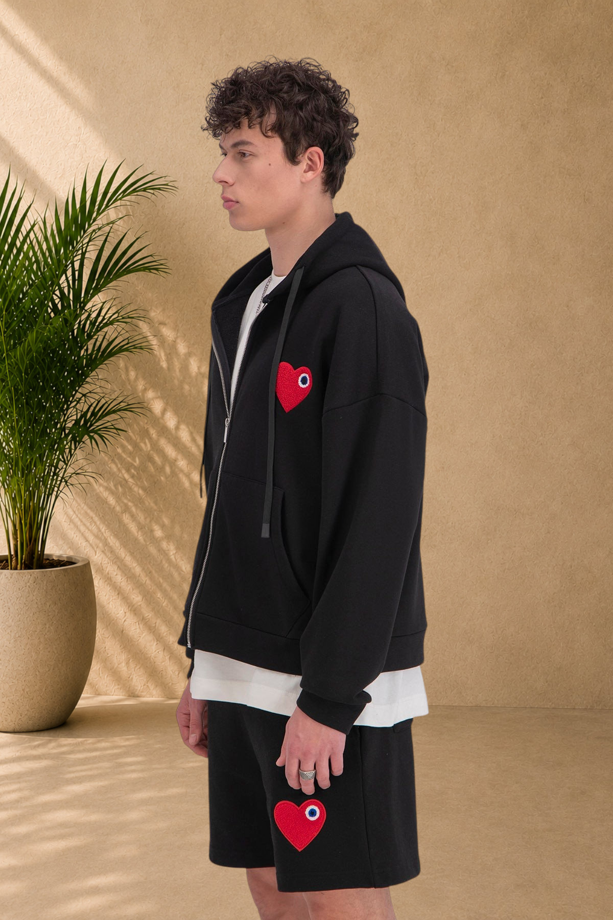 Stayin black zip-up hoodie with a red heart patch worn by a male model in profile view