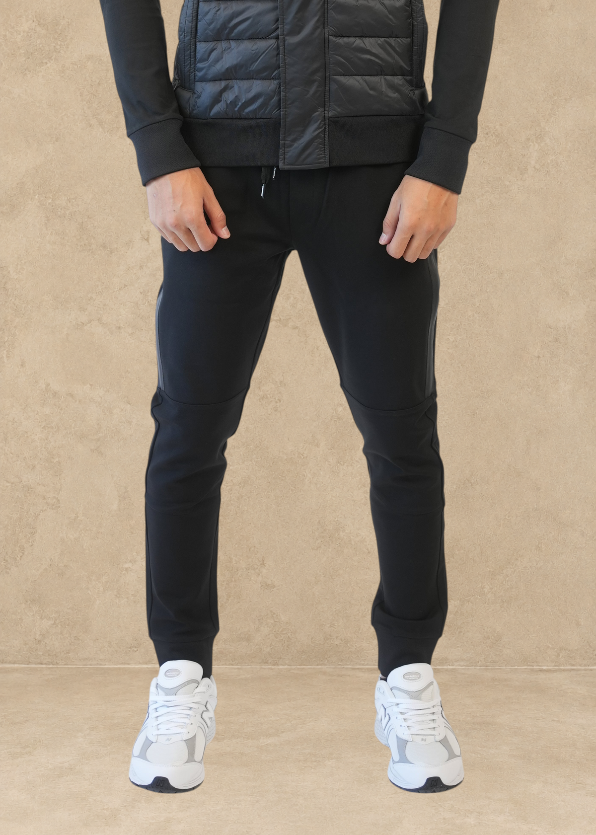 Pantalon jogging noir Helvetica Megeve porté par un homme avec une veste assortie et des baskets blanches Stayin