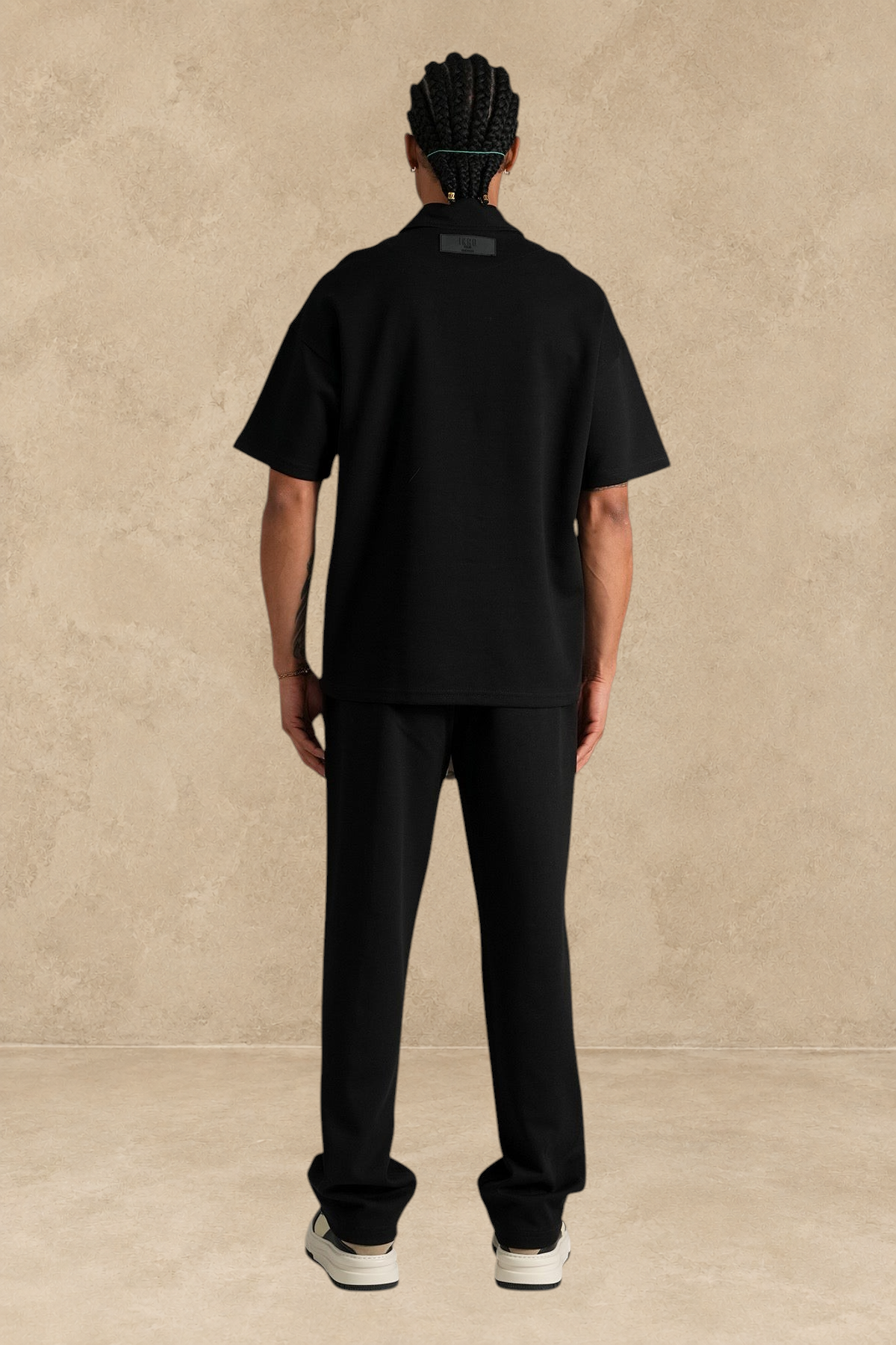 Vue arrière d'un mannequin portant un ensemble Stayin noir composé d'un polo zippé et d'un pantalon coupe large