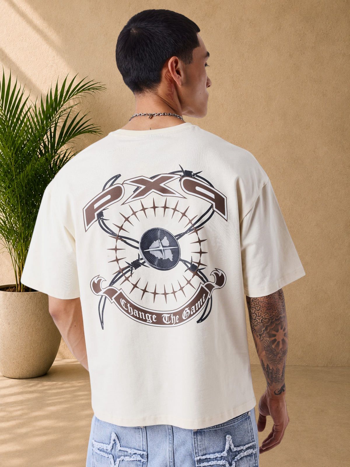 Stayin beige oversized cotton t-shirt with large graphic print on the back, worn by a man in a studio setting.