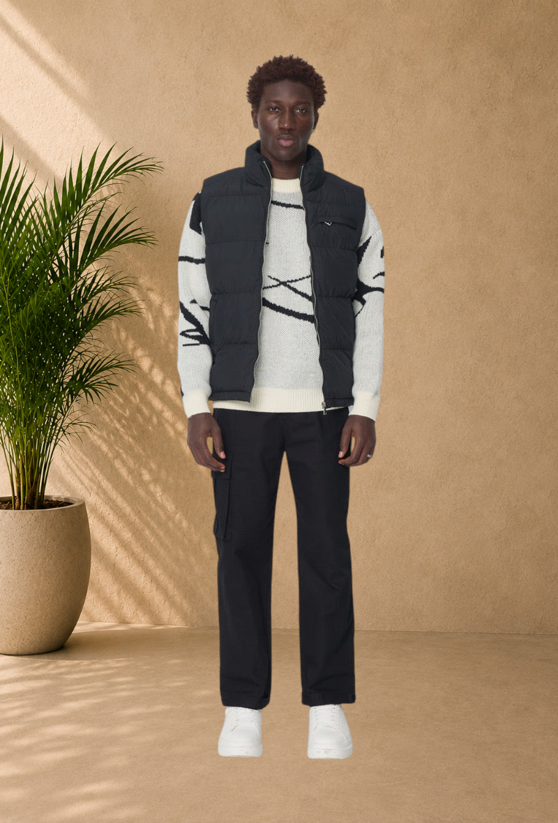 Stayin black sleeveless puffer vest with a high collar worn over a patterned sweater and black trousers