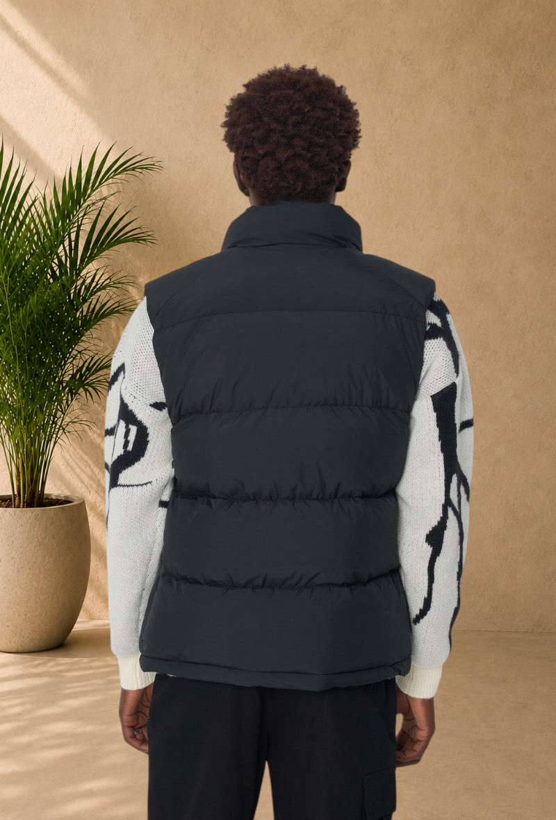 Stayin black sleeveless puffer vest with a high collar worn over a patterned knit sweater, back view.