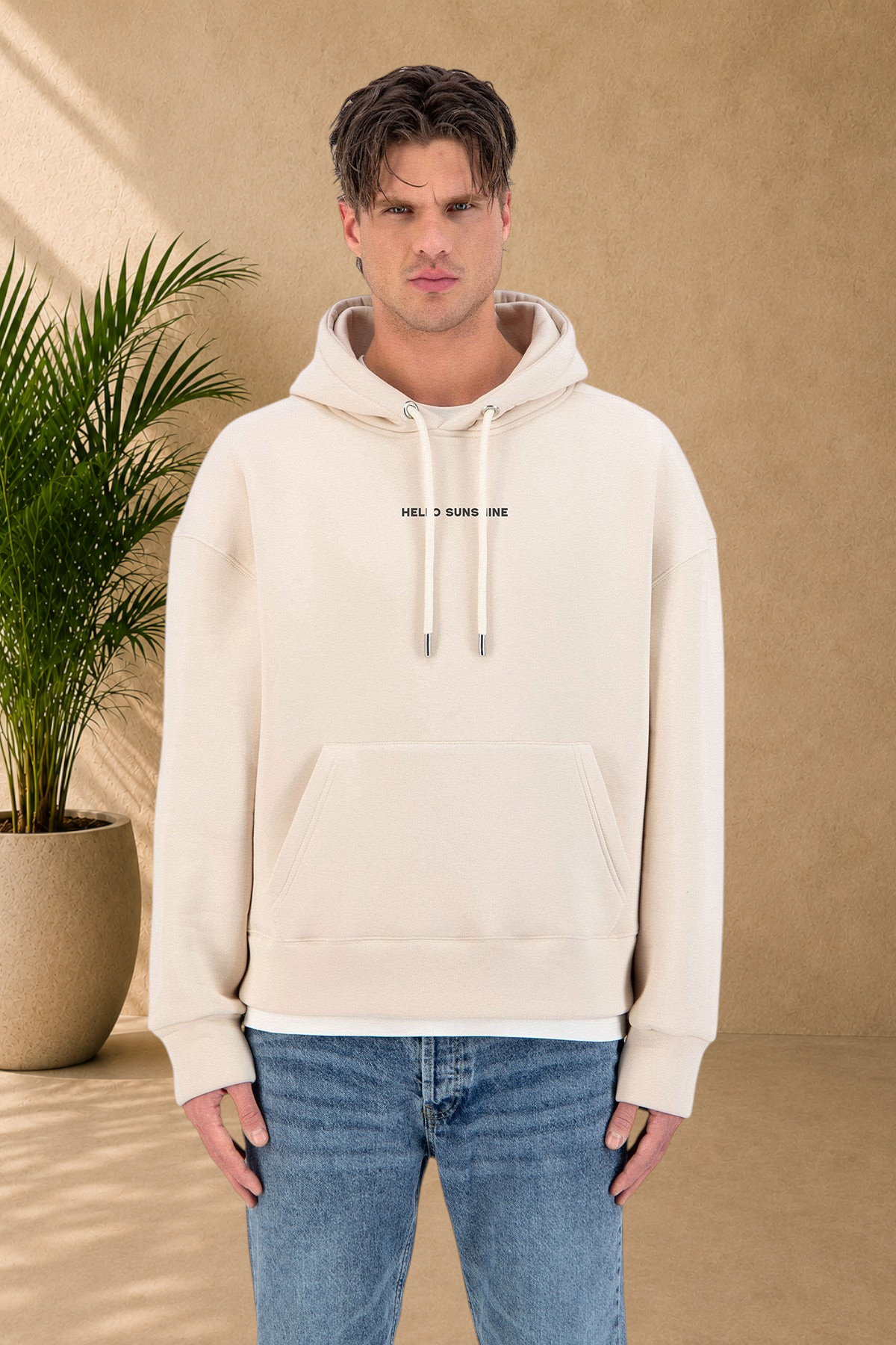 Stayin beige quilted hoodie with Hello Sunshine text, worn by a model in blue jeans against a white background.