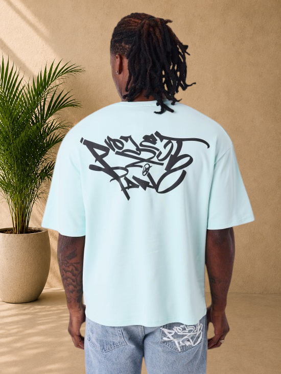 Stayin oversized light green cotton t-shirt with black graffiti graphic print on the back, worn by a man