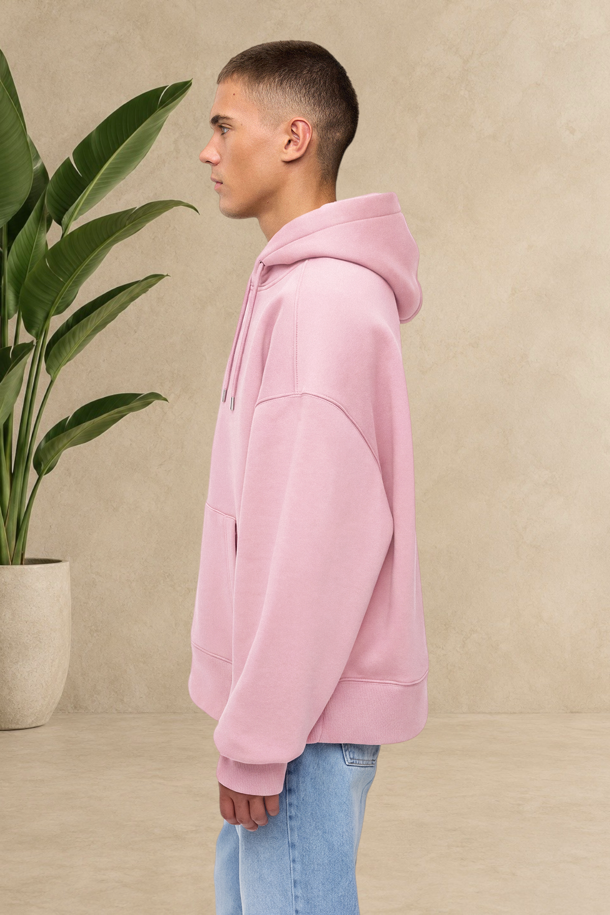 Sweat à capuche Stayin rose épais et matelassé porté de profil par un mannequin sur fond neutre avec une plante