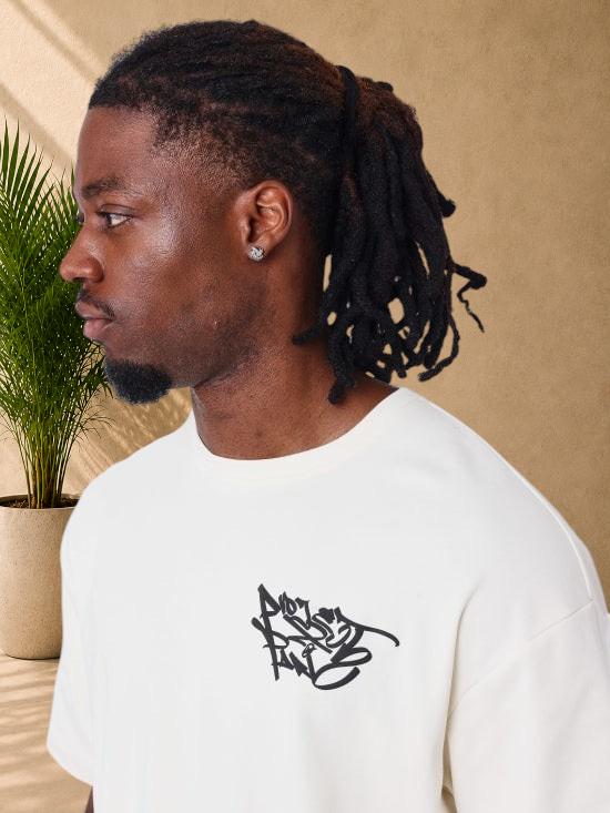 Stayin PXP beige oversized cotton t-shirt with black graffiti logo on the chest worn by a man in profile view