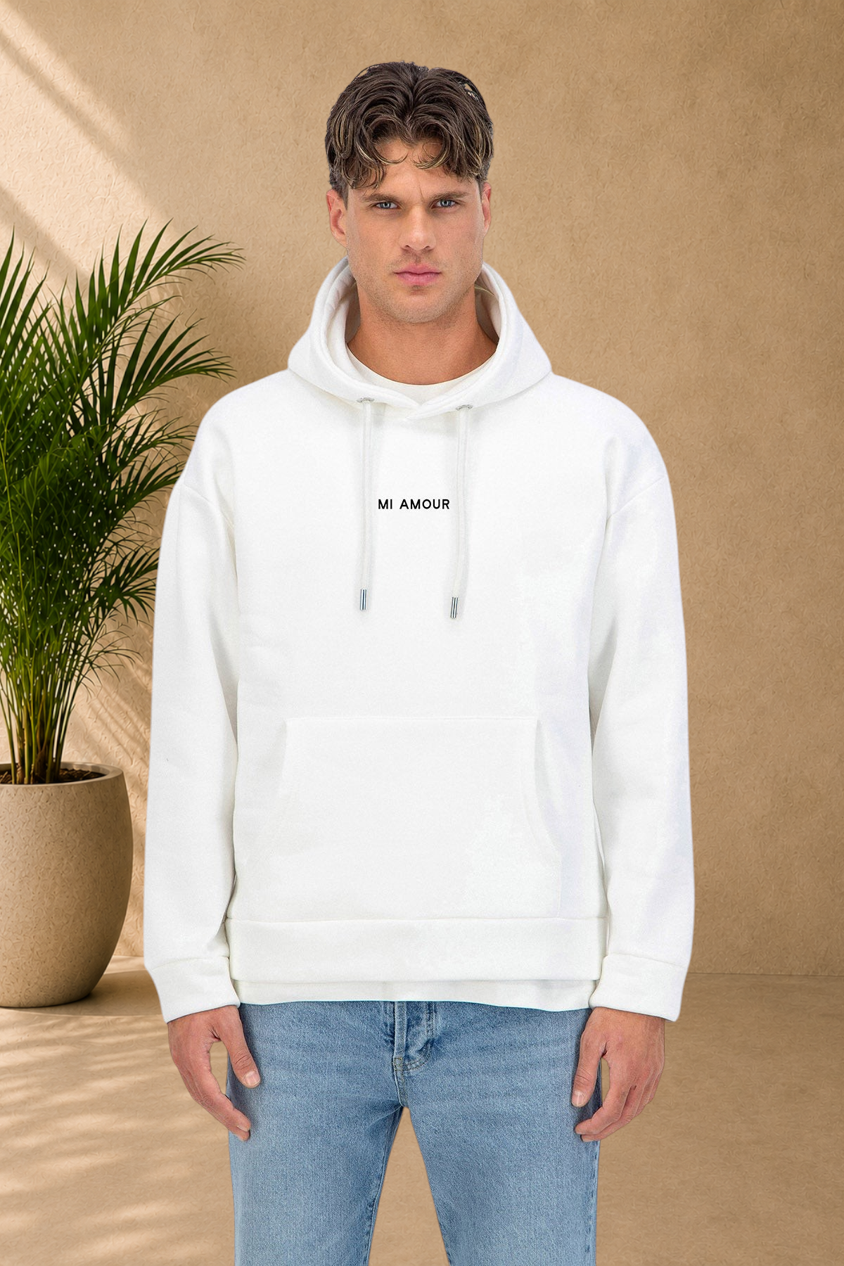 Stayin white quilted hoodie with Mi Amour text, worn by a male model in a studio setting with a potted plant.