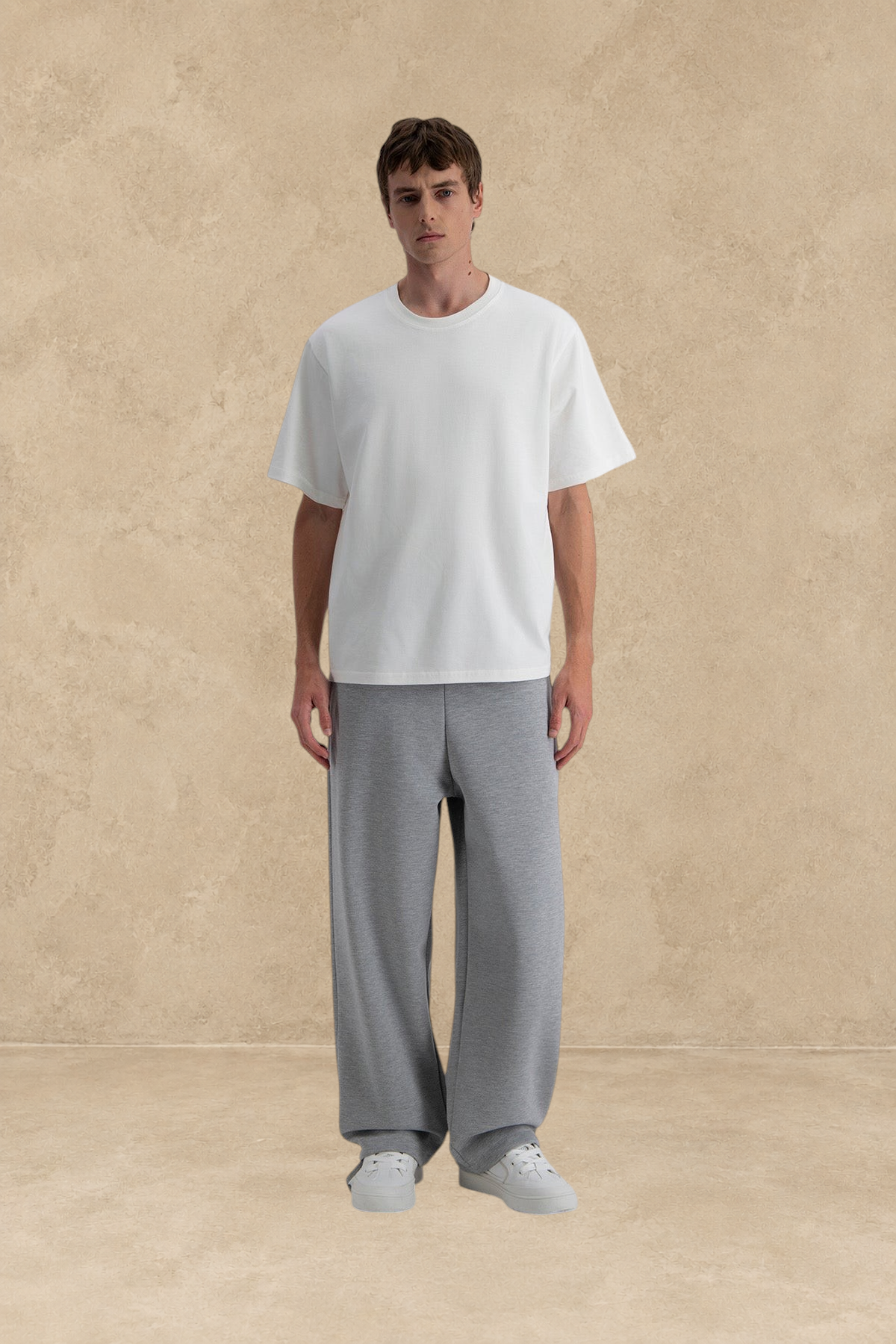 Mannequin portant un pantalon jogg loose gris Stayin avec un t-shirt blanc sur fond beige texturé