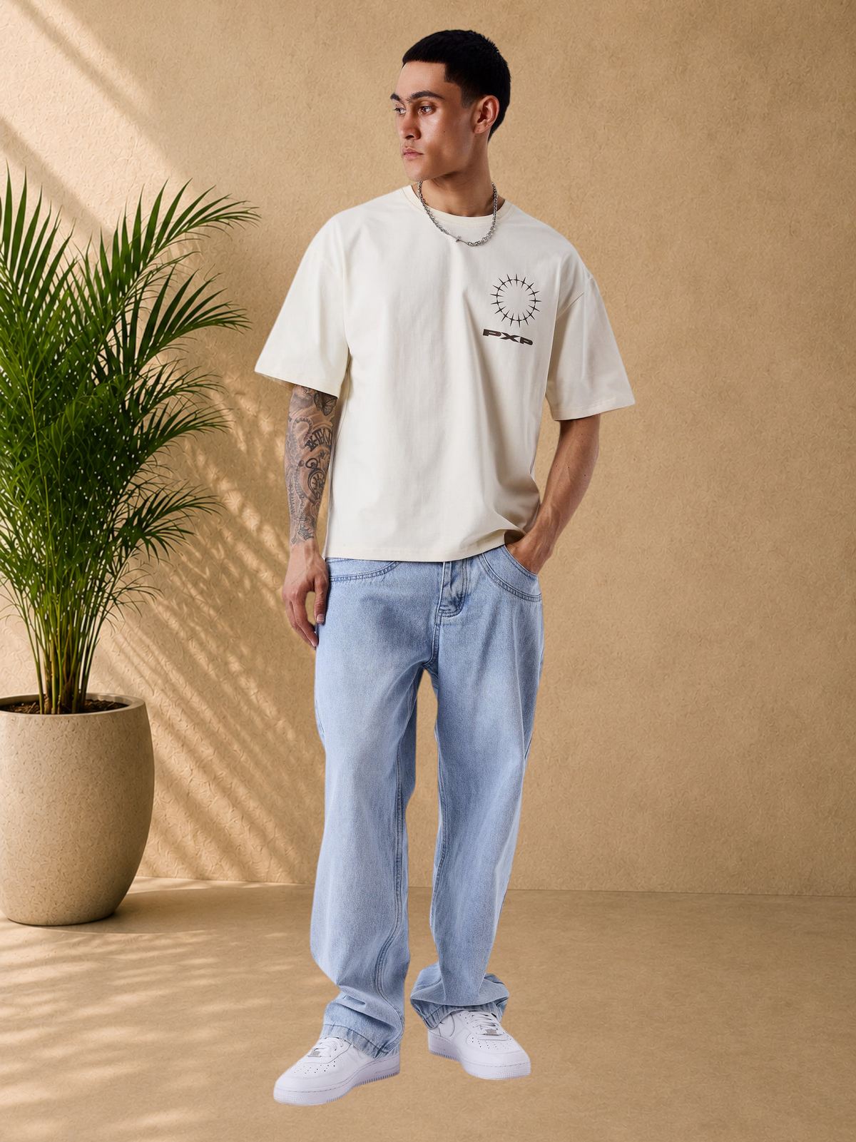 Stayin PXP beige oversized cotton t-shirt with graphic logo print on chest, worn by a model with light blue jeans.