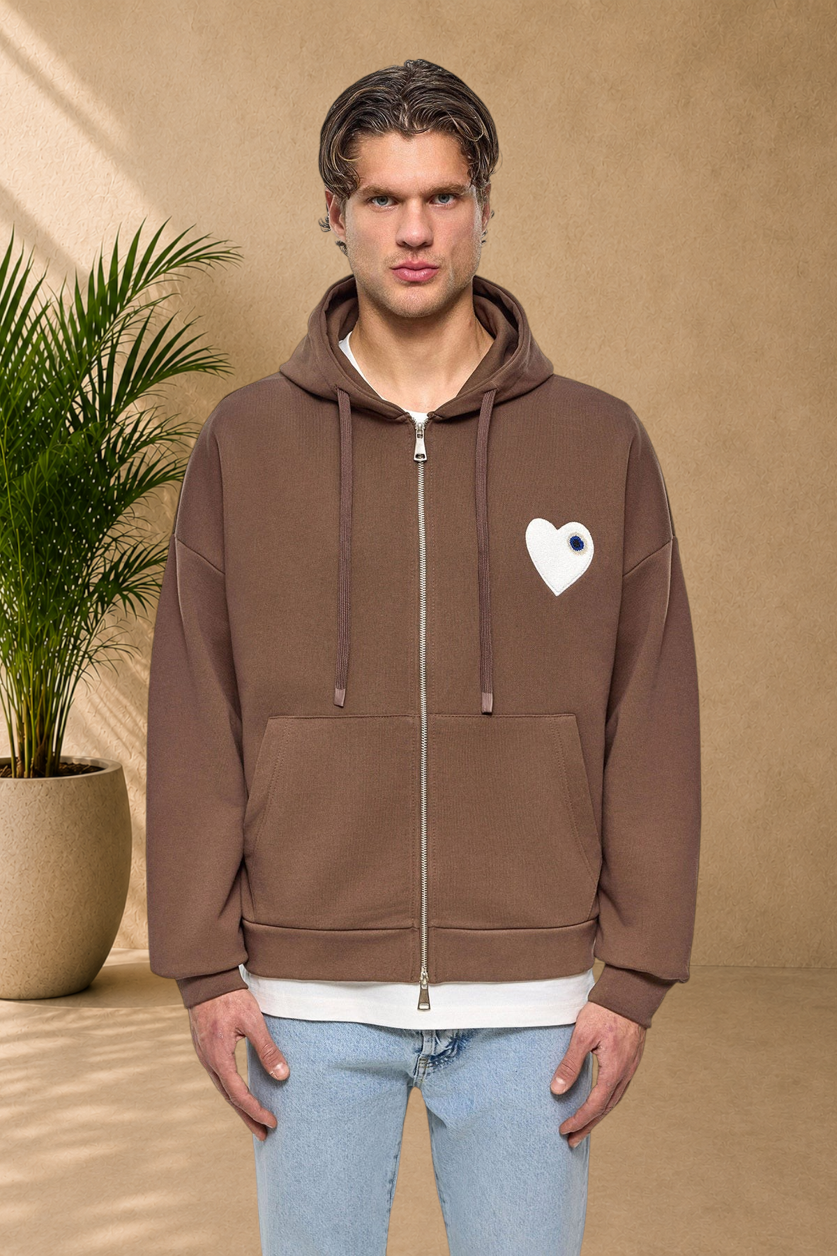Stayin brown zip-up hoodie with a white heart patch on the chest worn by a male model