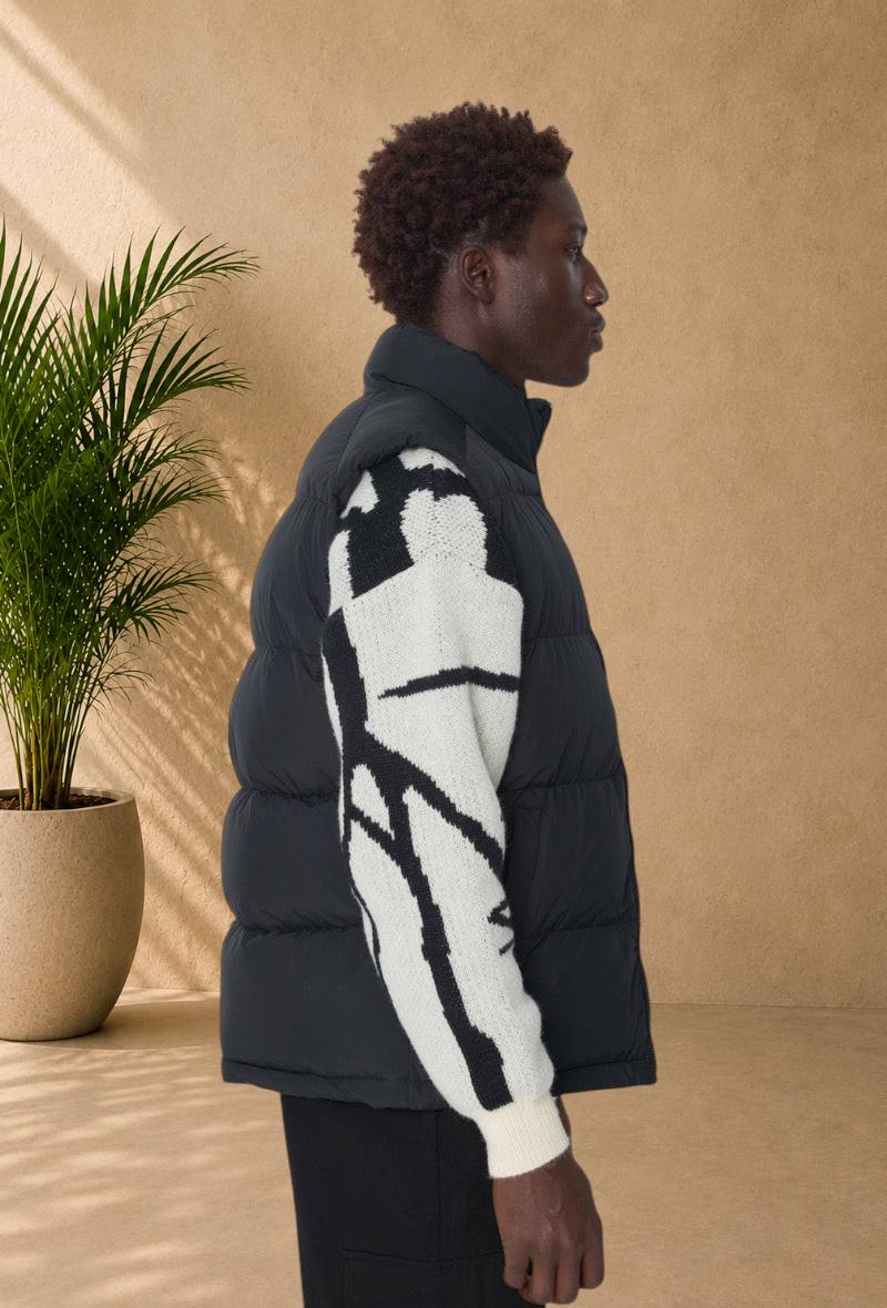 Stayin black sleeveless puffer vest with a high collar worn by a model over a patterned knit sweater