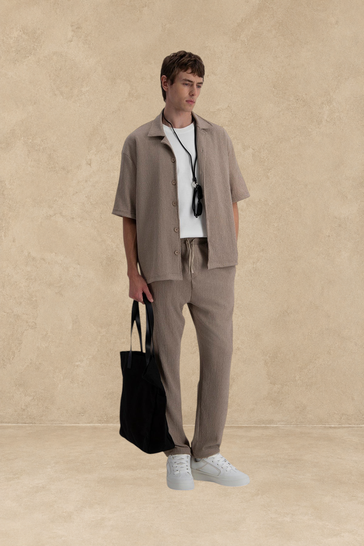 Homme portant un pantalon plissé marron Stayin avec une chemise assortie et un sac fourre-tout noir