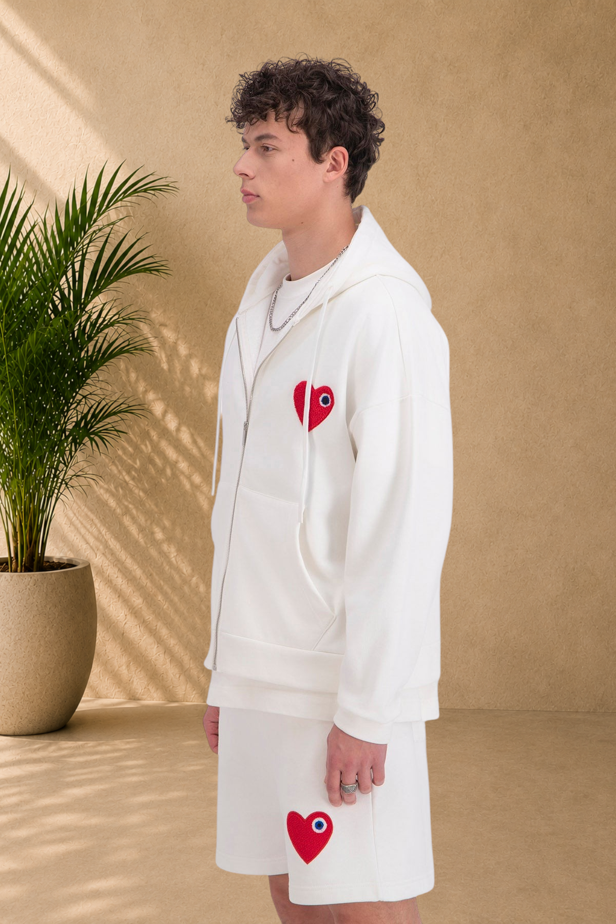 Stayin white zip-up hoodie with a red heart patch worn by a model in profile view