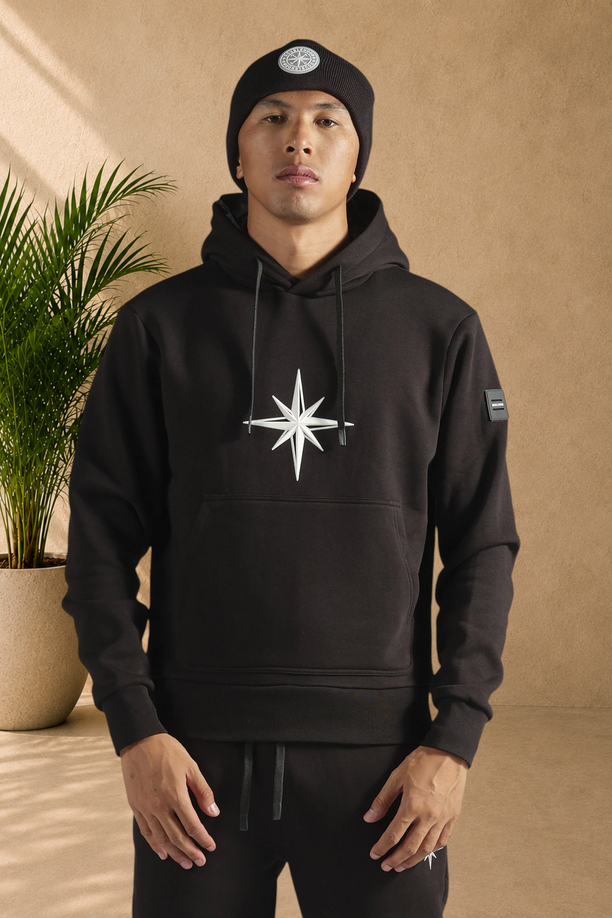 Stayin black doublehood sweatshirt with a white compass star logo, worn by a man in a matching beanie