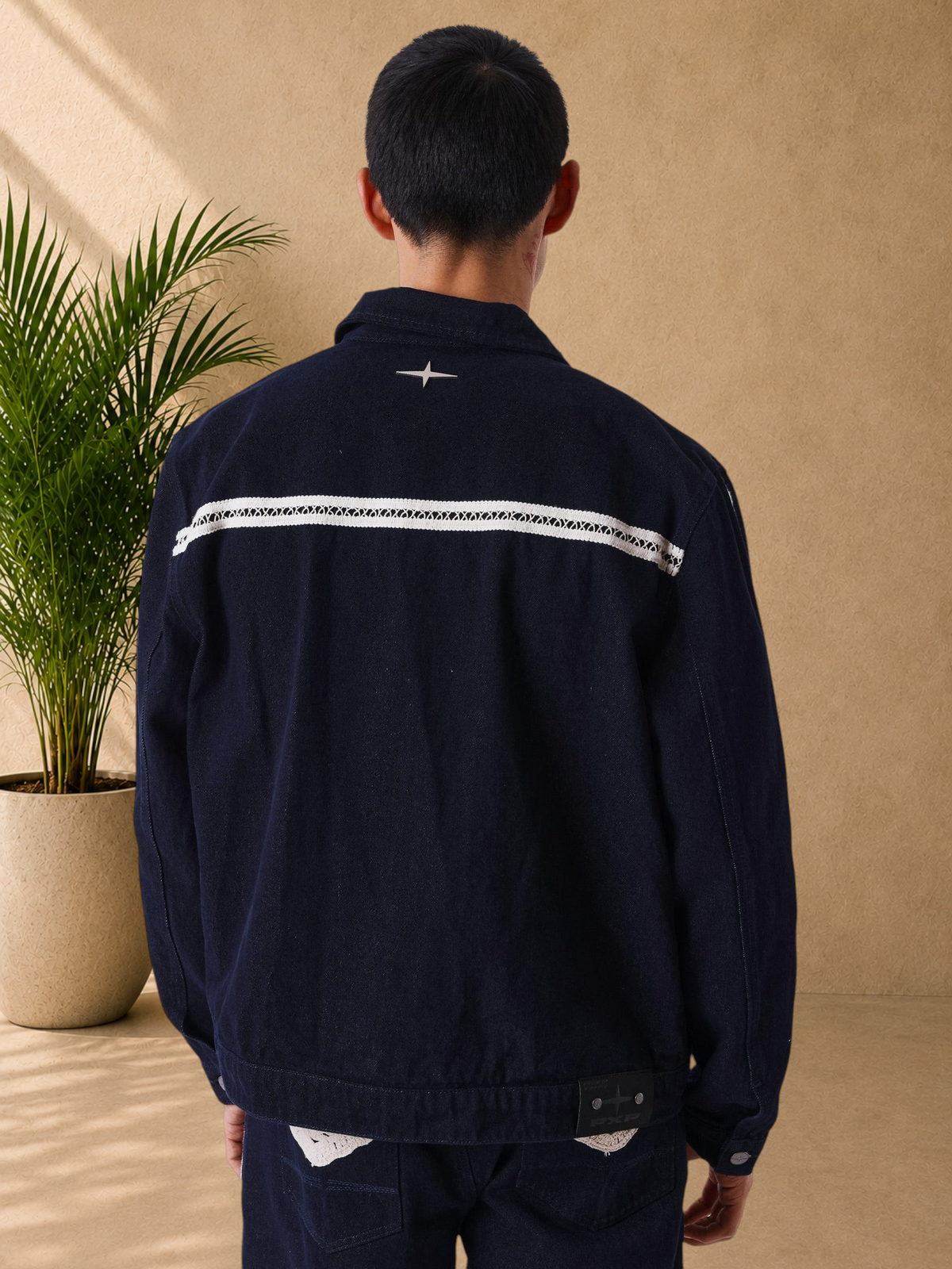 Stayin PXP black denim jacket with beige crochet stripe detail on the back, worn by a model, back view.