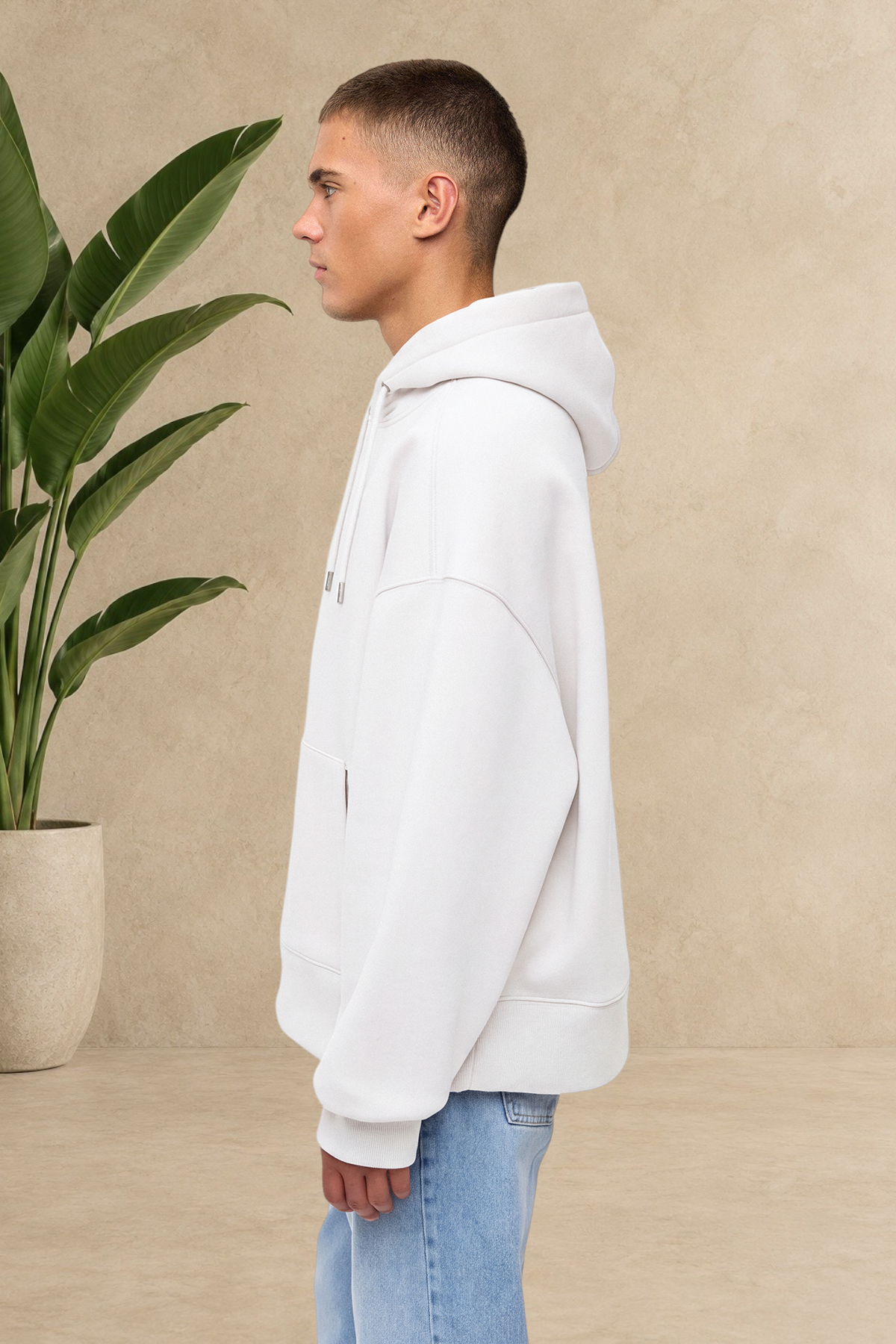 Homme portant un sweat à capuche blanc Stayin épais et matelassé, vue de profil, devant une plante verte