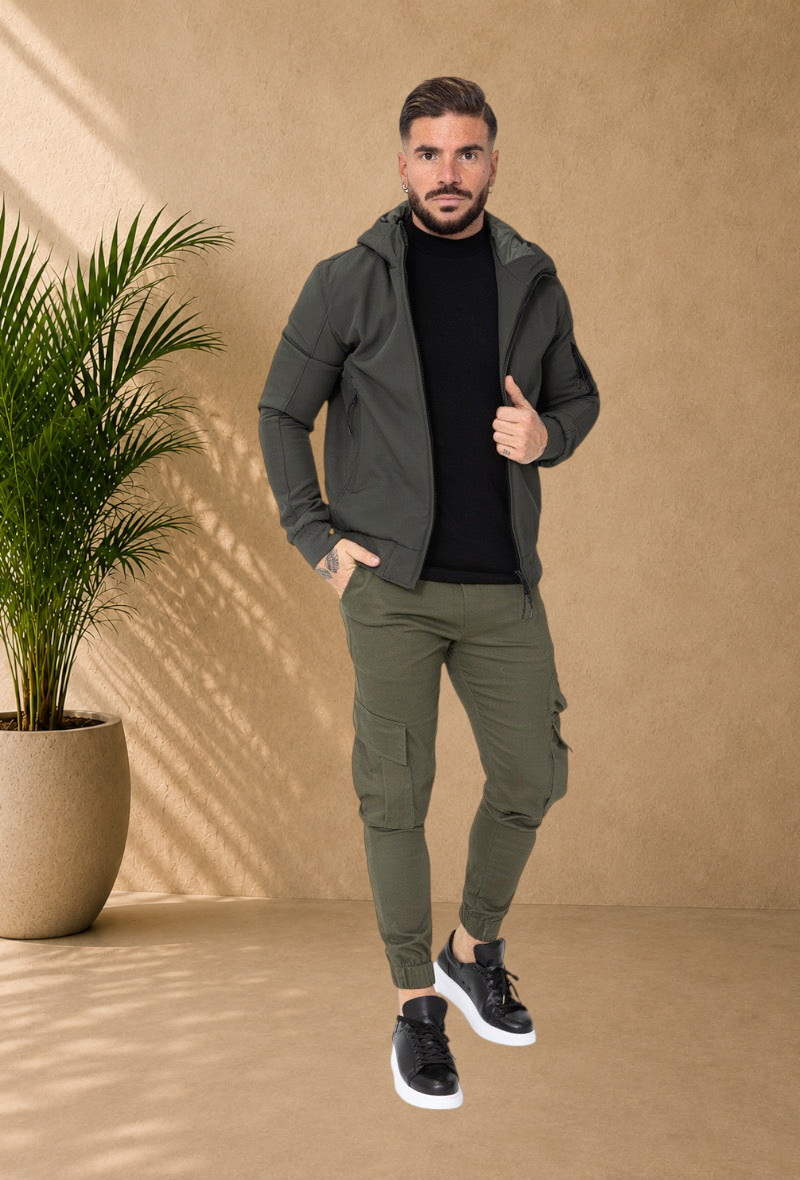 Stayin model wearing a fitted khaki hooded windbreaker jacket with matching cargo joggers and black sneakers