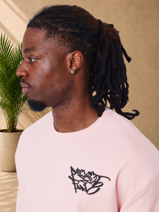 Stayin PXP oversized pink cotton t-shirt with black graffiti logo on chest worn by a man in profile view