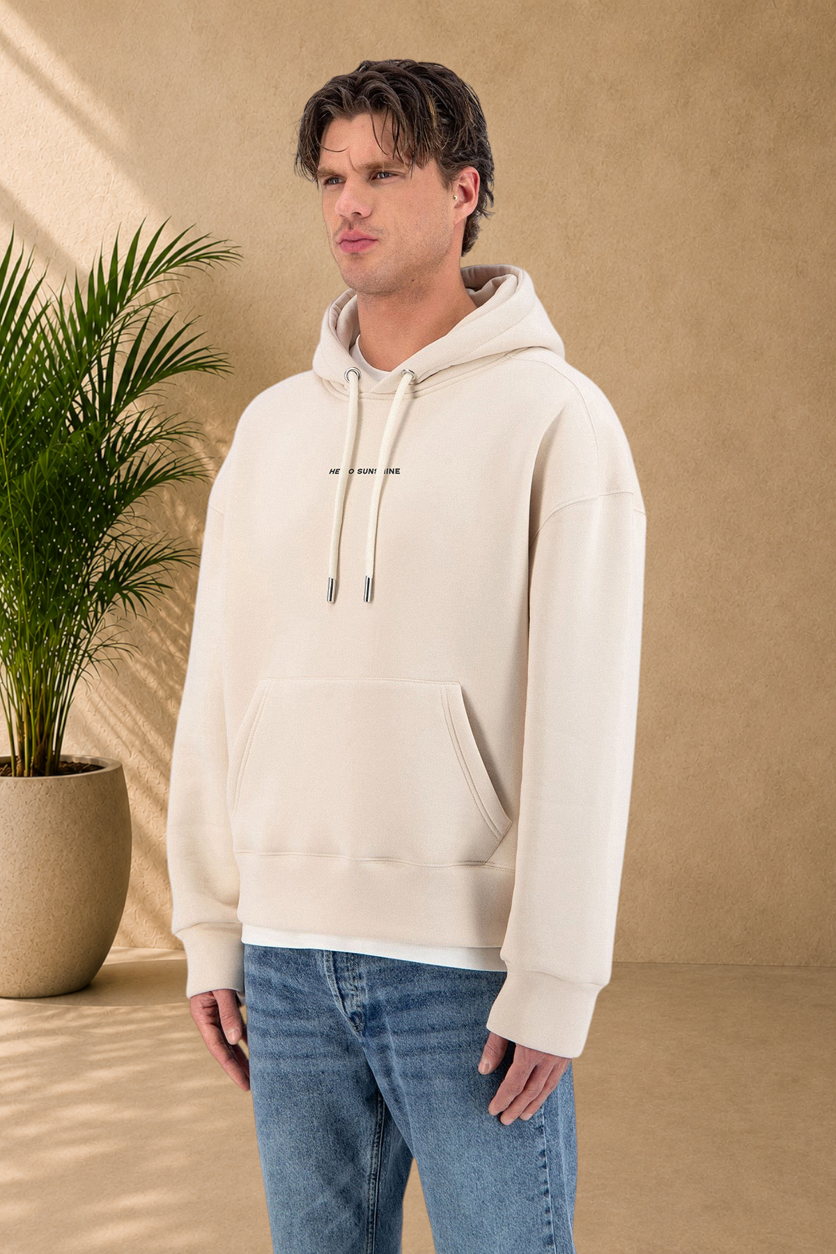 Stayin beige quilted hoodie with drawstring hood and Sunshine text detail worn by a male model with blue jeans